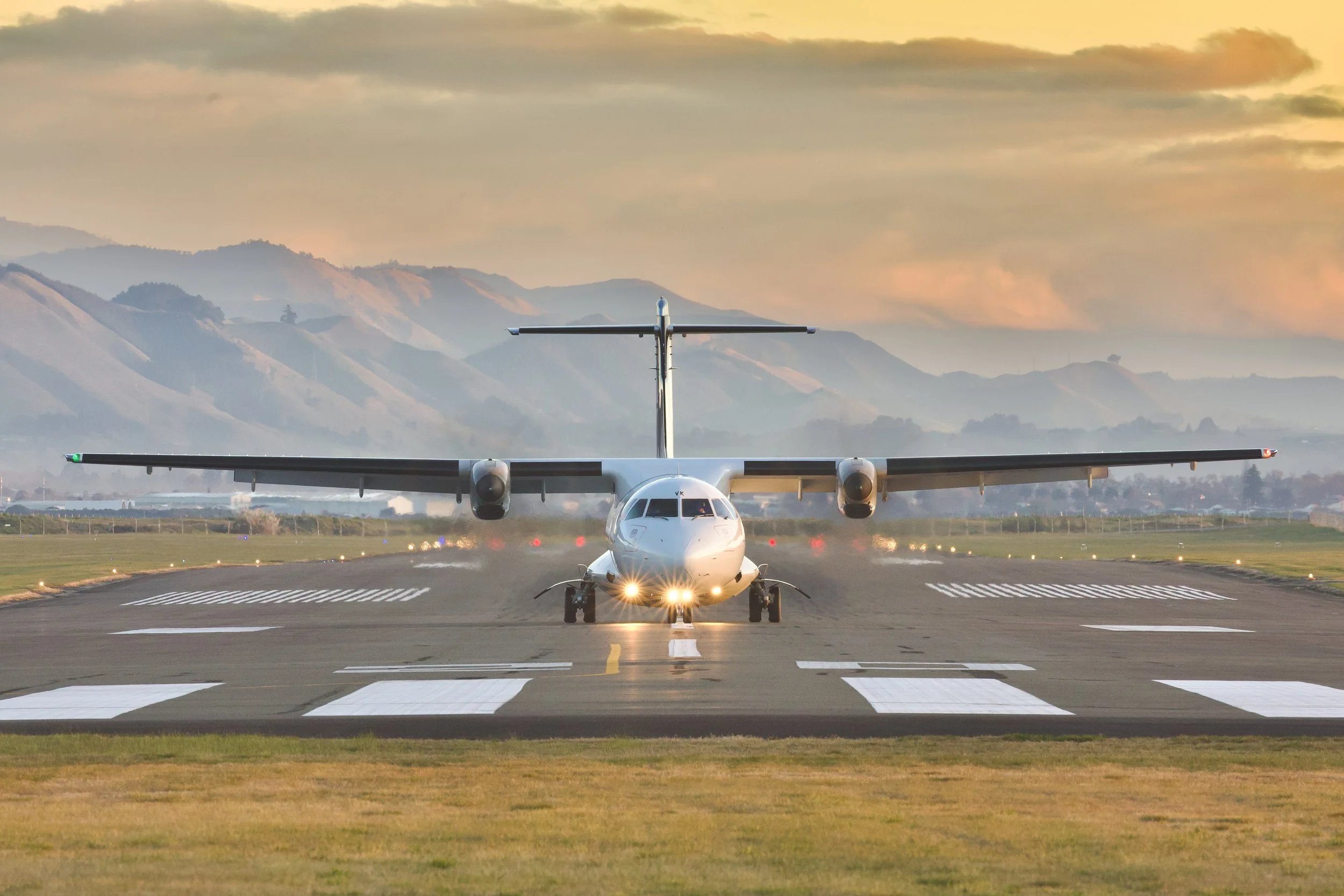 Twin-engine turboprop passenger plane on a runway at sunset with mountains in the background