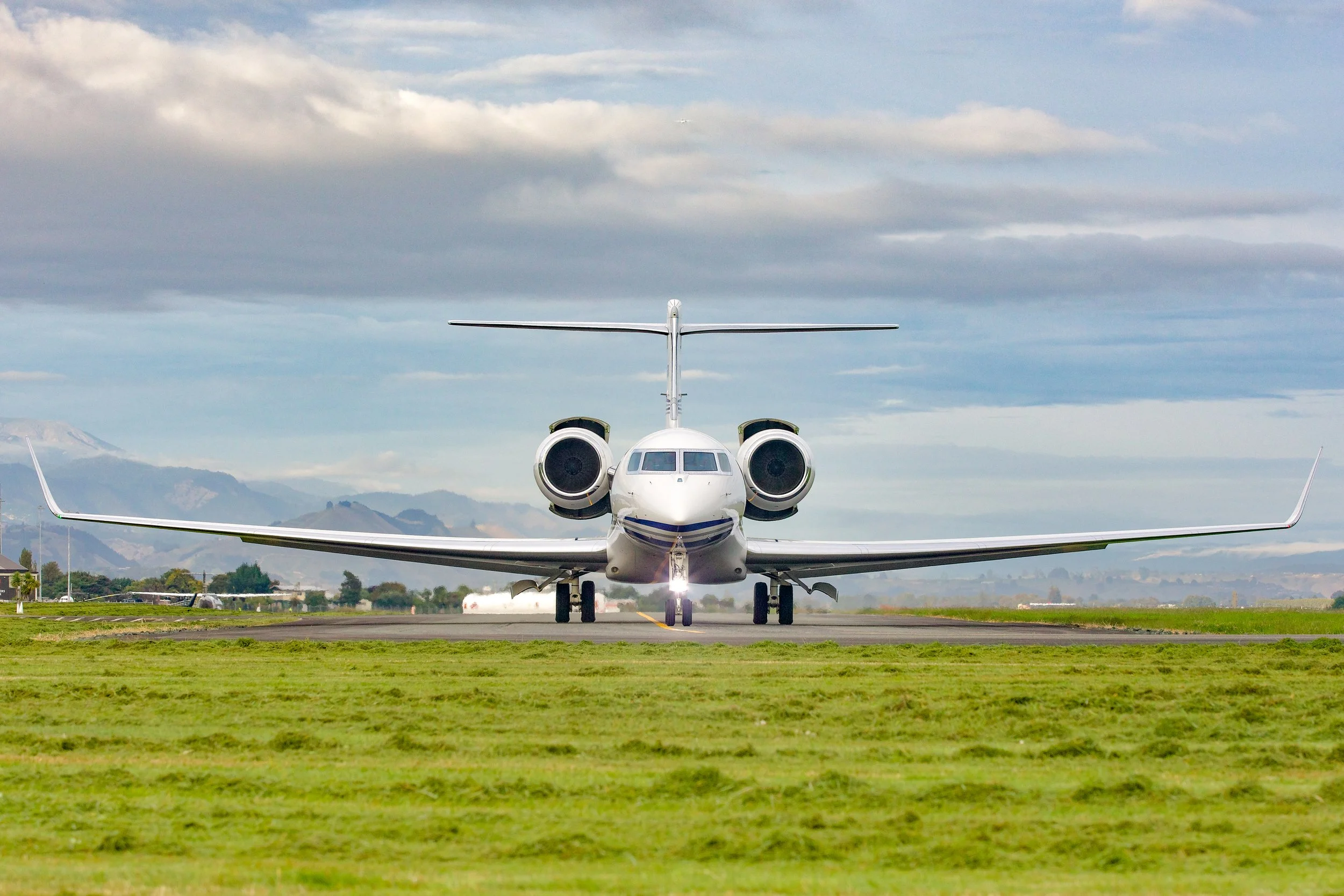 Private jet facing the camera on an airport runway with mountains and cloudy sky in the background