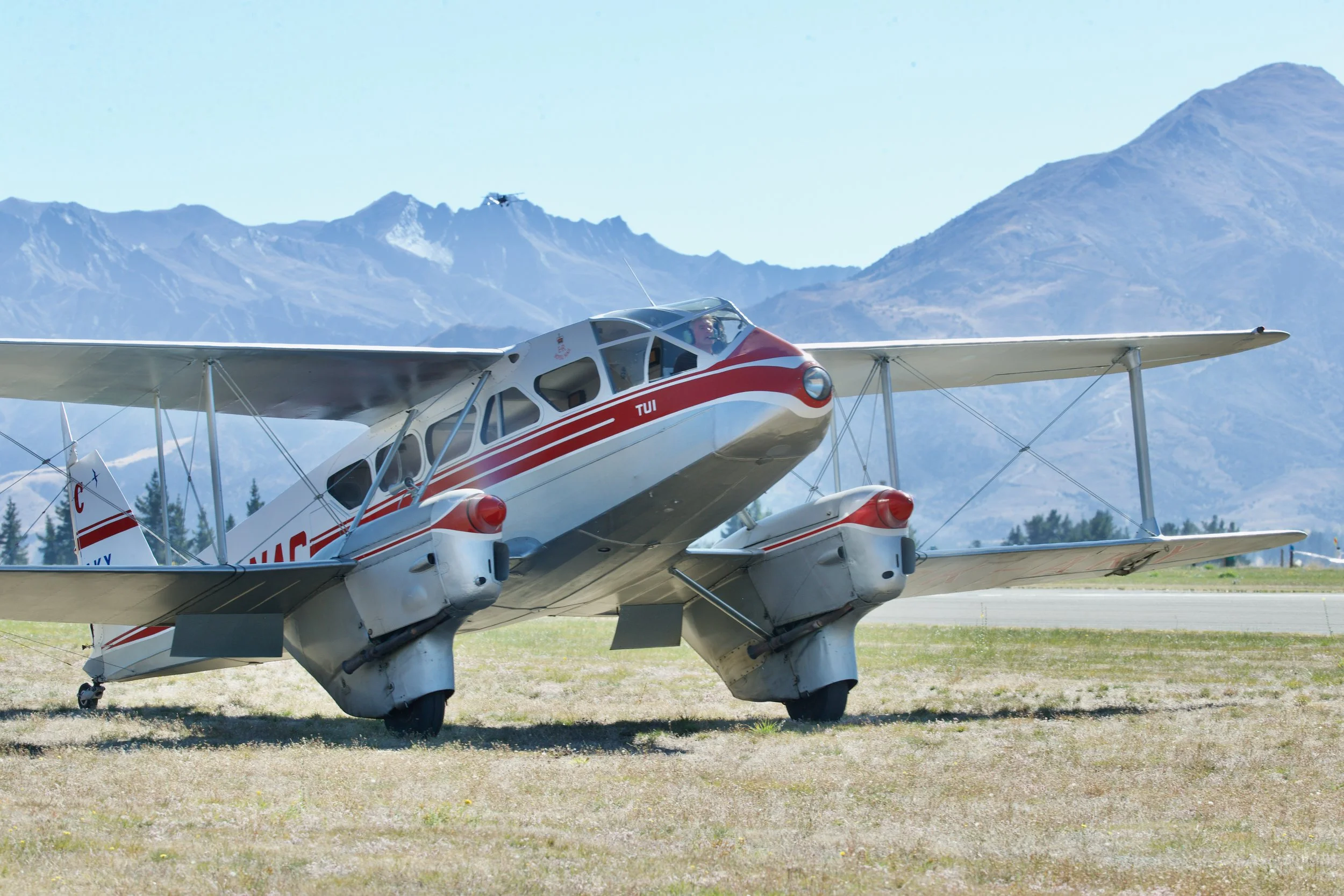 Vintage red-and-white twin-engine airplane parked against a mountainous landscape