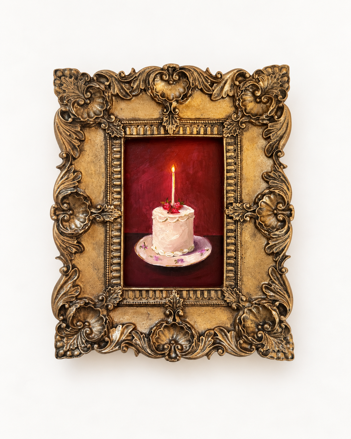 Ornate gold baroque frame surrounding a small white birthday cake with a lit candle on a plate