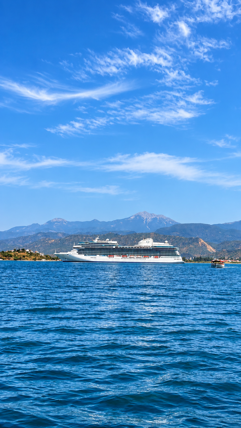 White cruise ship sailing on blue sea with mountains and wispy clouds in the background