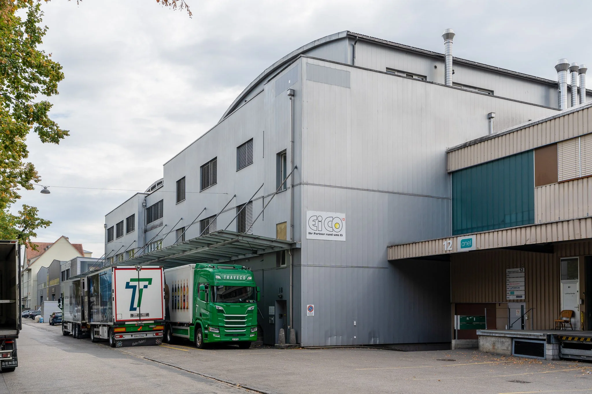 Industriegebäude mit Lüftungsschornsteinen, Eico-Firmenschild und geparkten Lieferwagen in einem Gewerbegebiet