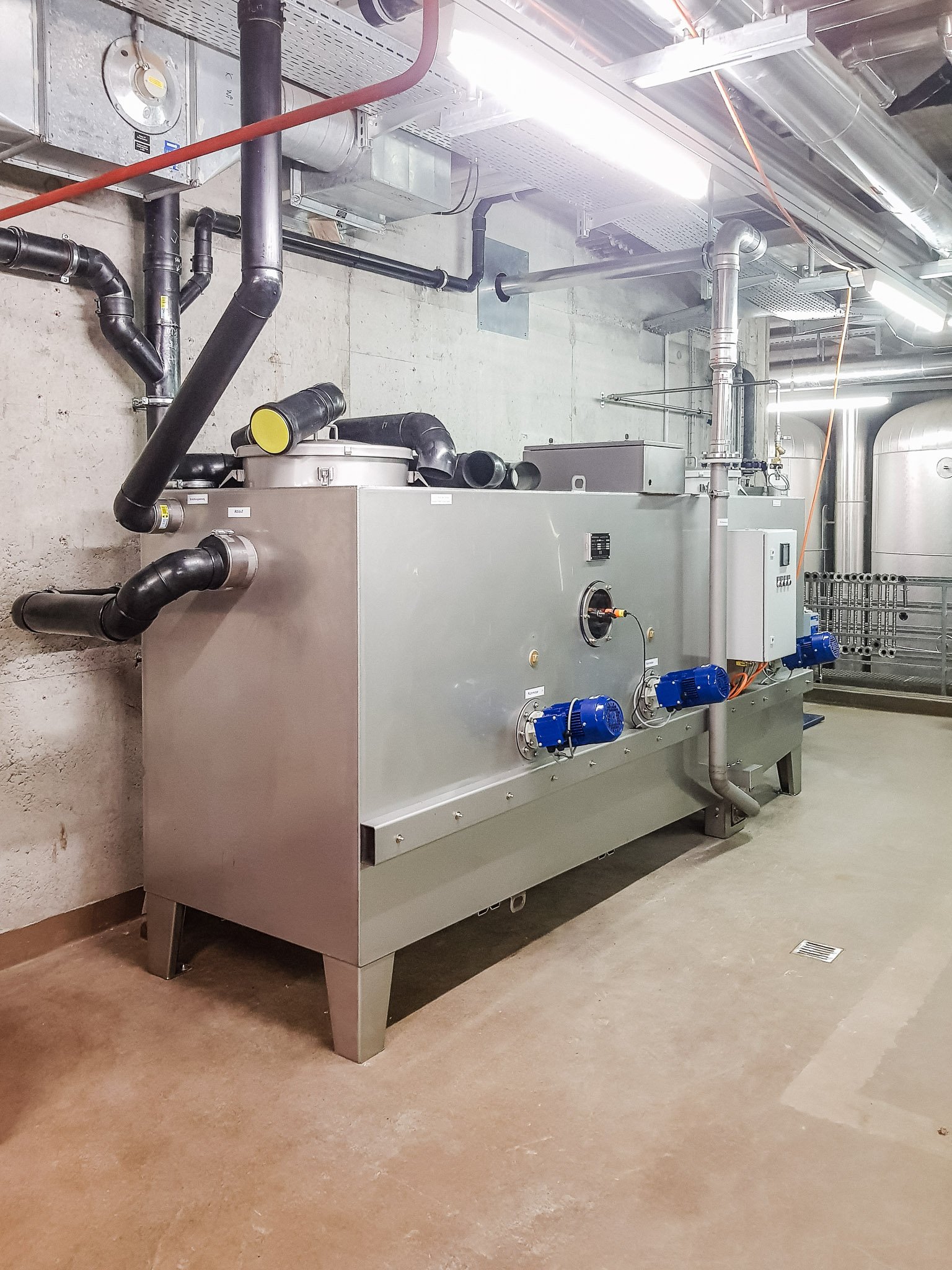 Technische Gebäudetechnik mit großer Heizungs- oder Lüftungsanlage, Rohrleitungen, Pumpen und Lüftungskanälen in einem Kellerraum