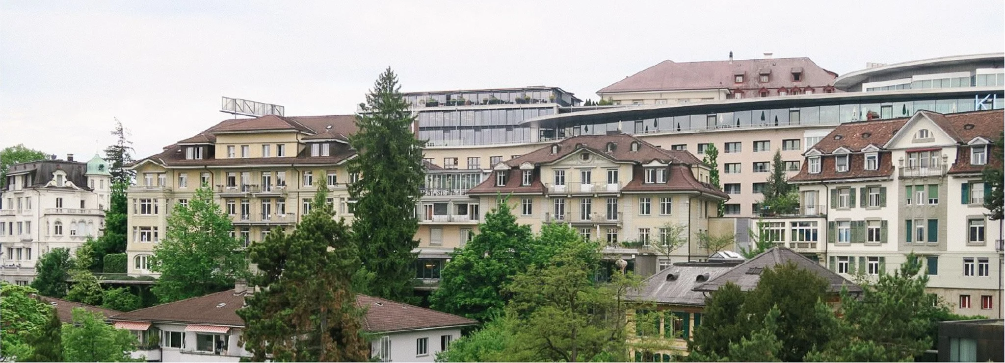 Stadtansicht mit historischen Wohnhäusern, Bäumen und modernen Gebäuden im Hintergrund