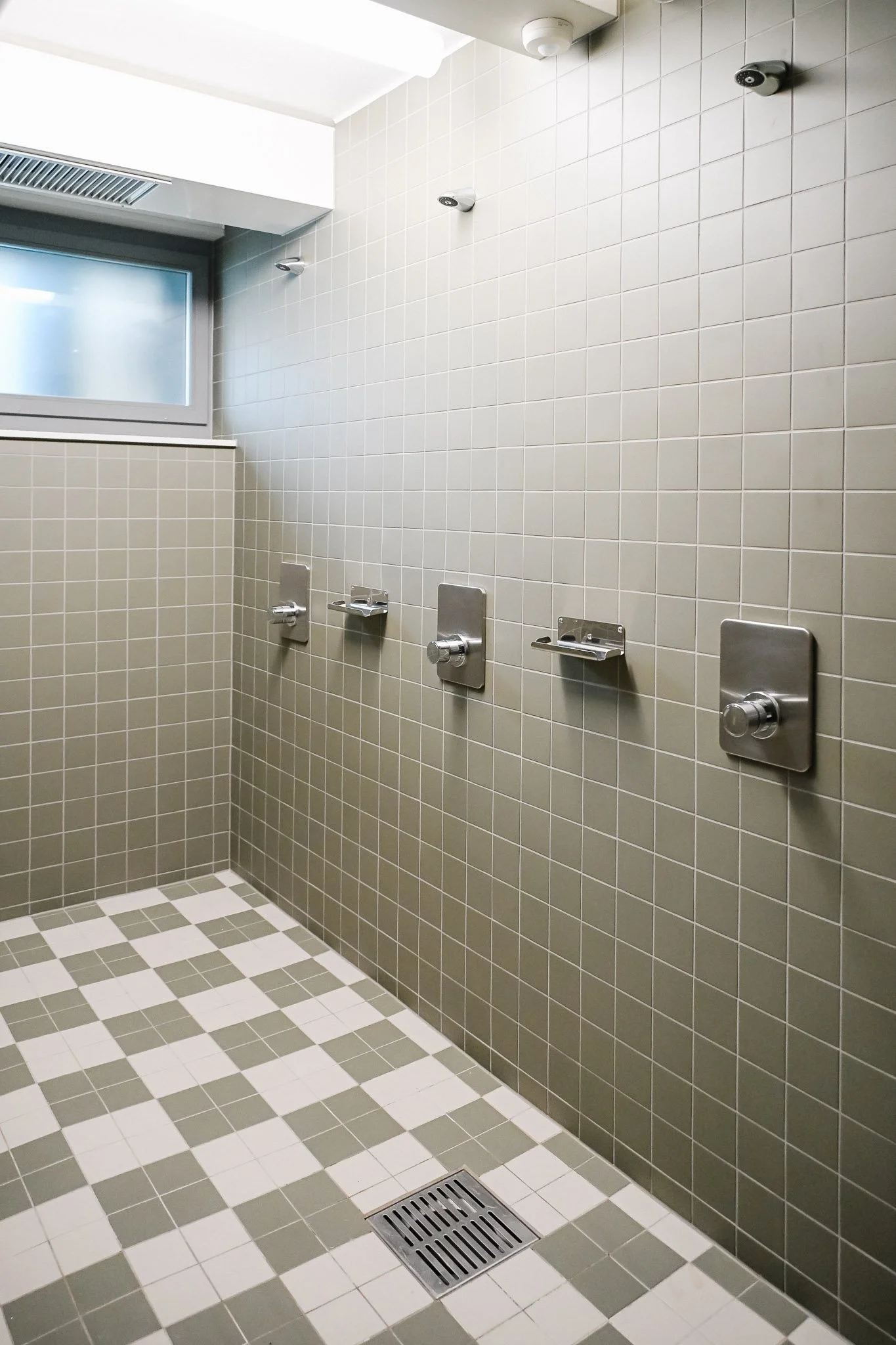 Barrierefreie Gemeinschaftsdusche mit mehreren Duscharmaturen, gefliesten Wänden, Fenster und Bodenablauf