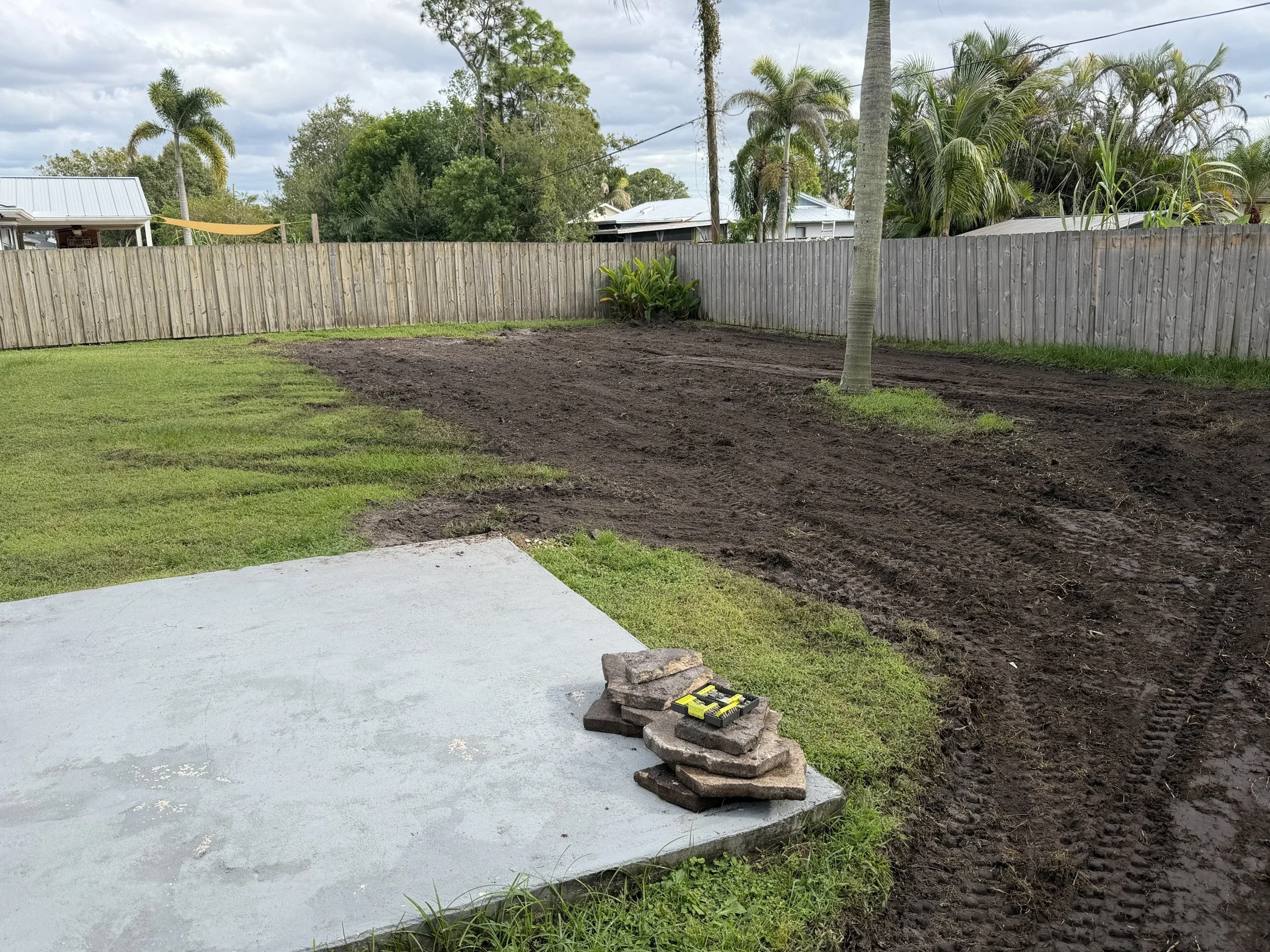 Ground preparation and material spreading around a backyard concrete slab.