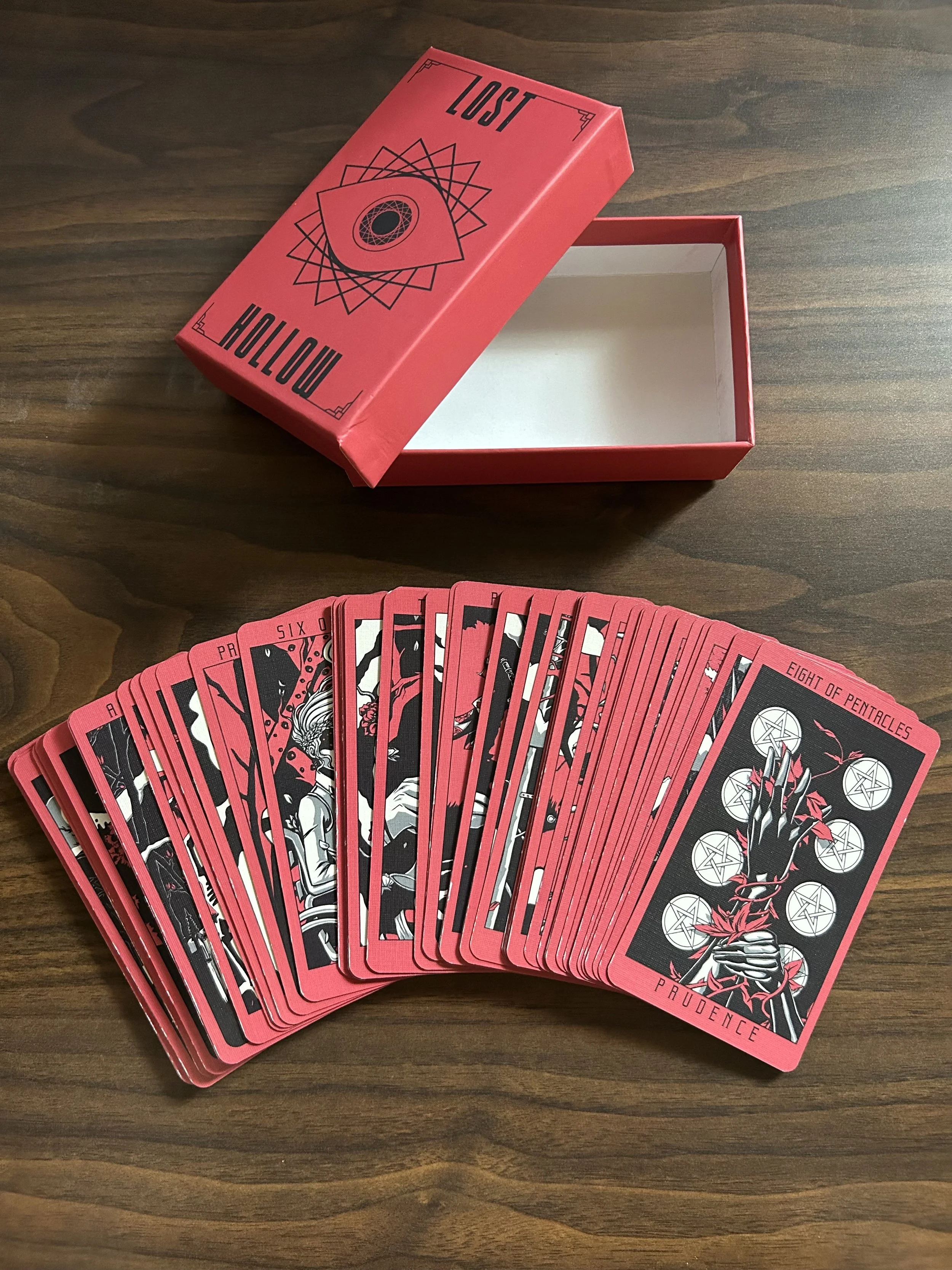 Red and black tarot cards fanned beside an open red tarot card box on a wooden table