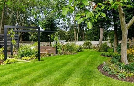 Landscaped backyard garden with manicured lawn, raised beds, pergola, mature trees, and flower borders