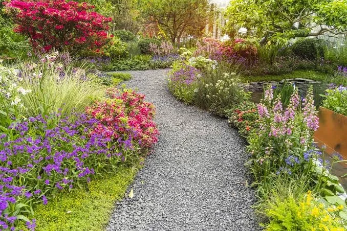 Colorful landscaped garden with a winding gravel path, flowering plants, ornamental grasses, shrubs, and a small pond