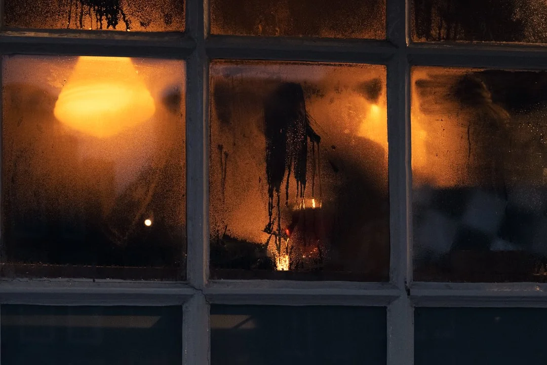 Rain-speckled window panes glowing with warm orange light at night