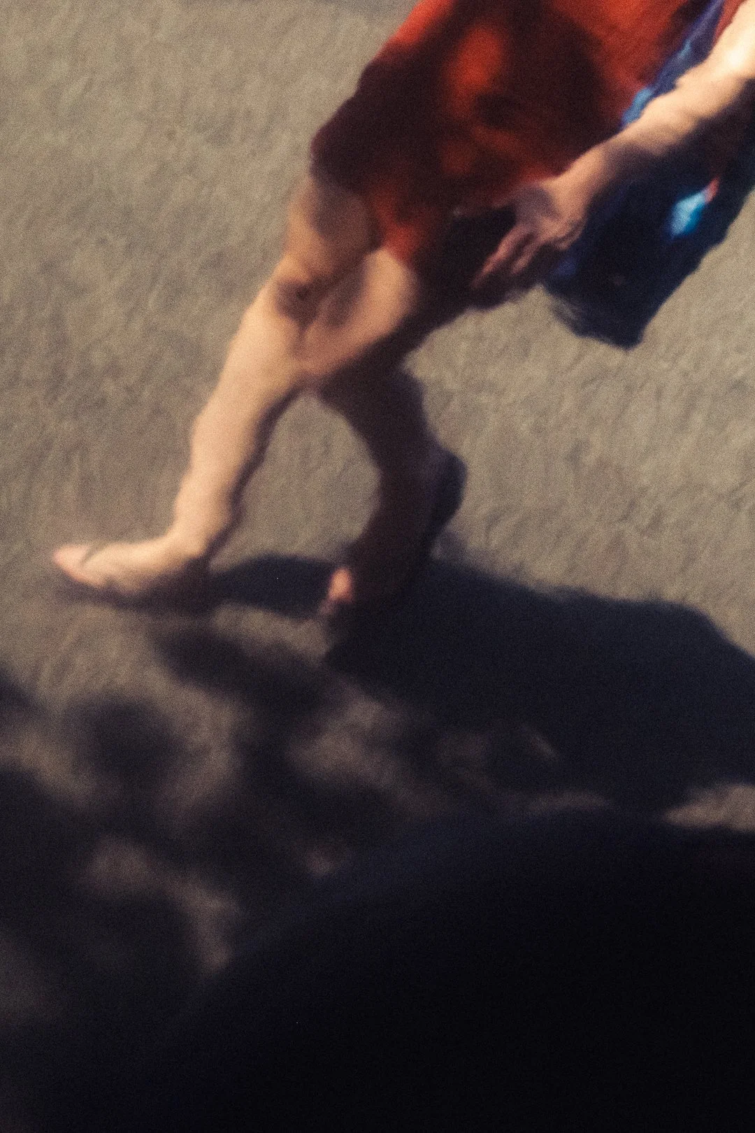 Blurry overhead view of a person in a red shirt walking on pavement.