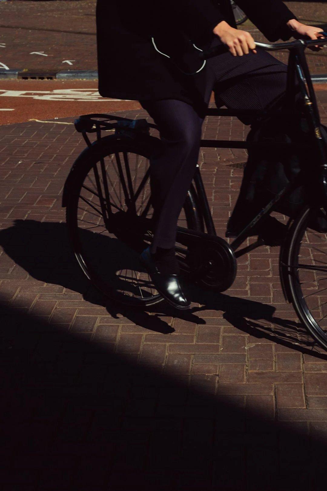 Close-up of a person riding a black bicycle on a sunlit brick street.
