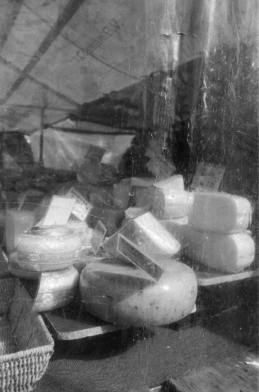 Black-and-white photo of packaged cheeses and labeled cheese wheels displayed in a shop window.