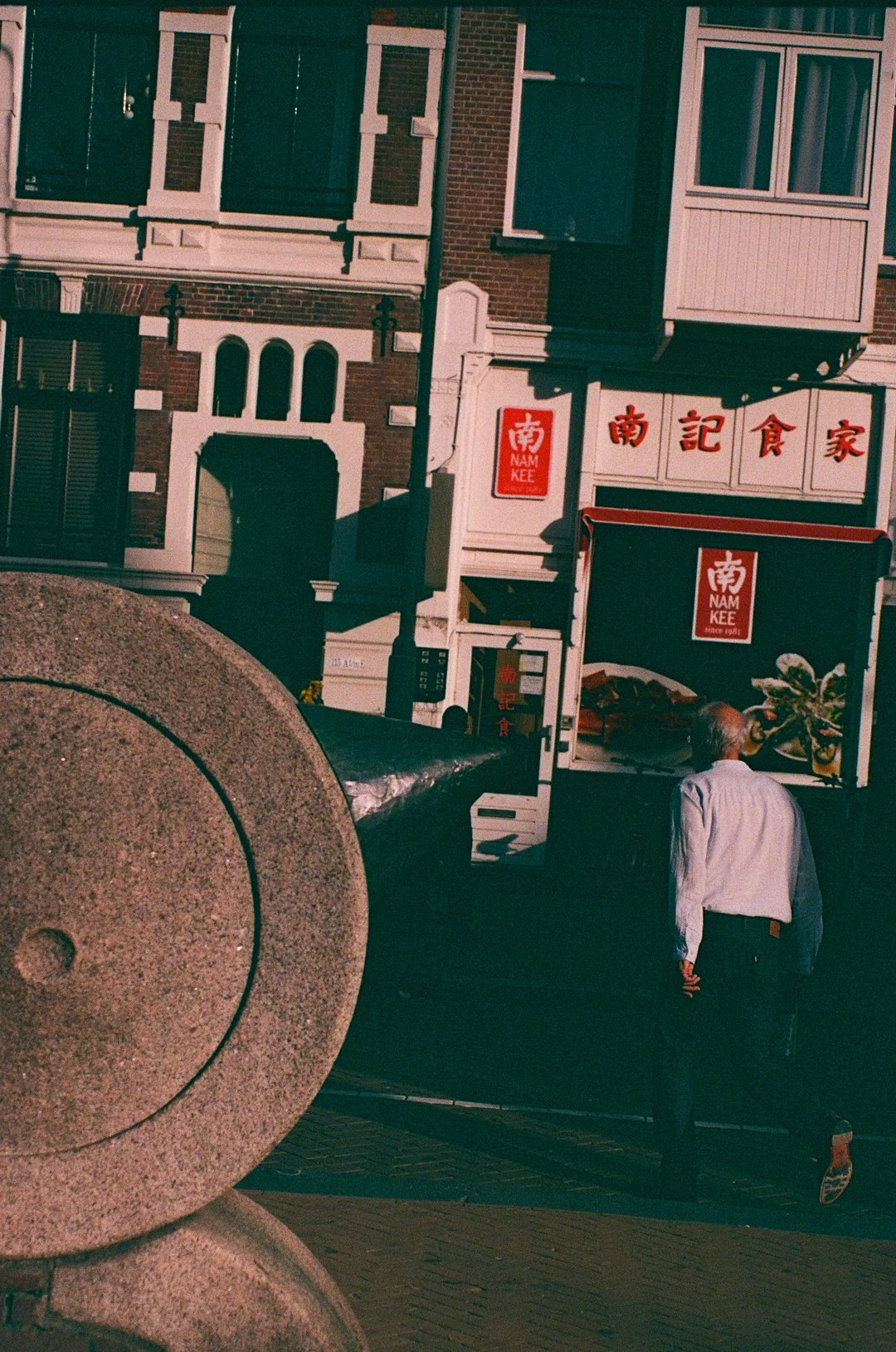Nam Kee Chinese restaurant storefront on a city street, with Chinese characters on the sign and a pedestrian walking past.