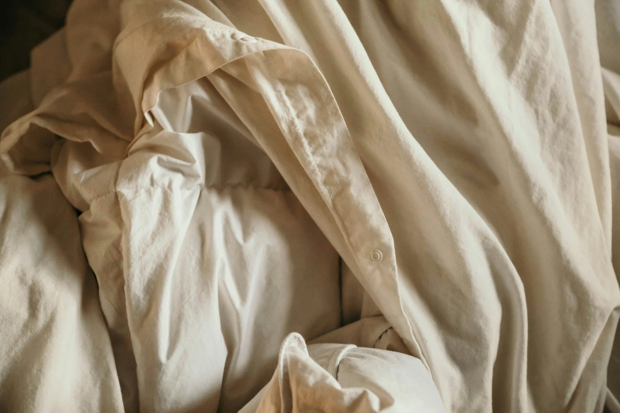 Close-up of wrinkled cream-colored fabric with overlapping folds and buttons.