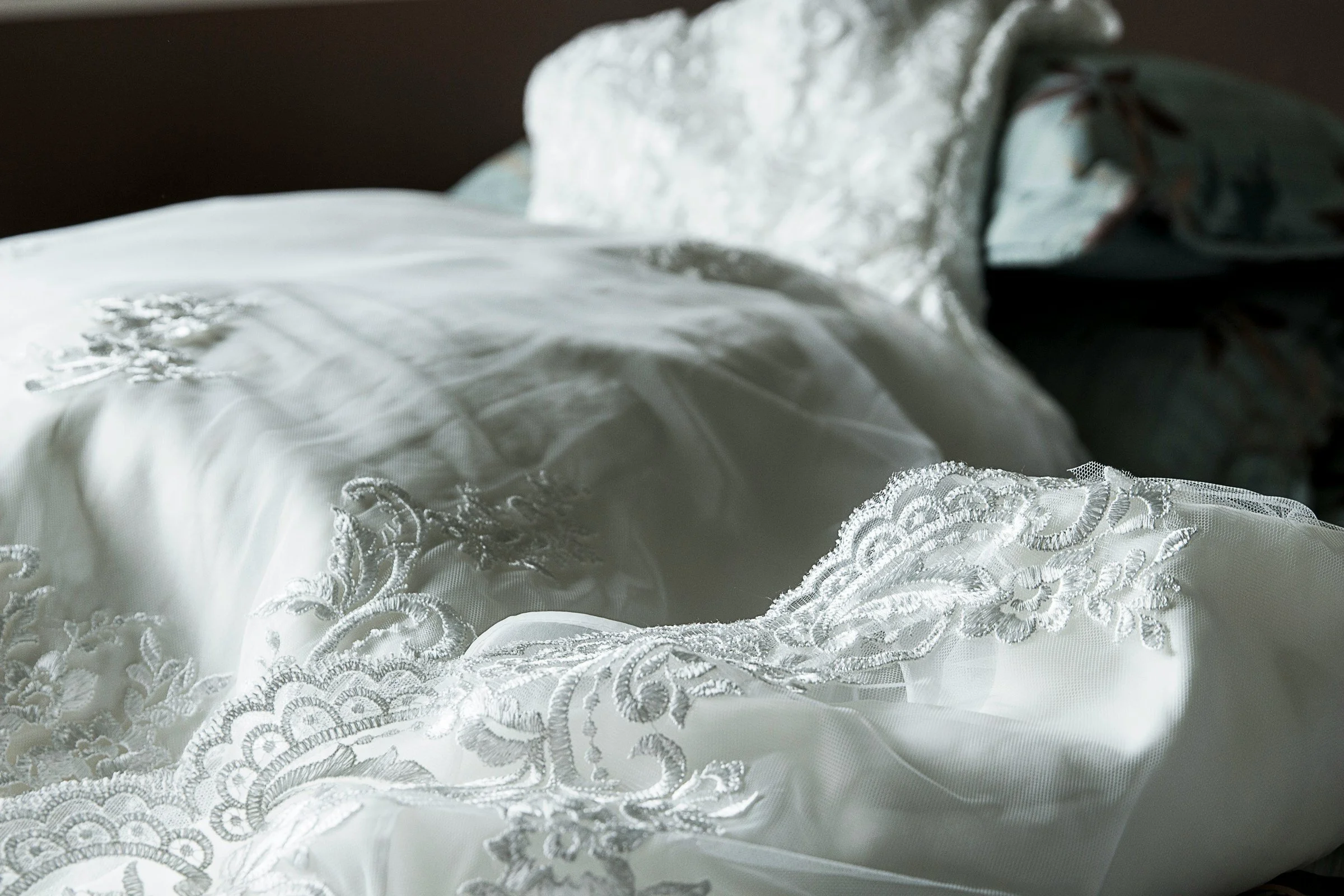 Close-up of an elegant white wedding dress with intricate lace embroidery and sheer tulle fabric.