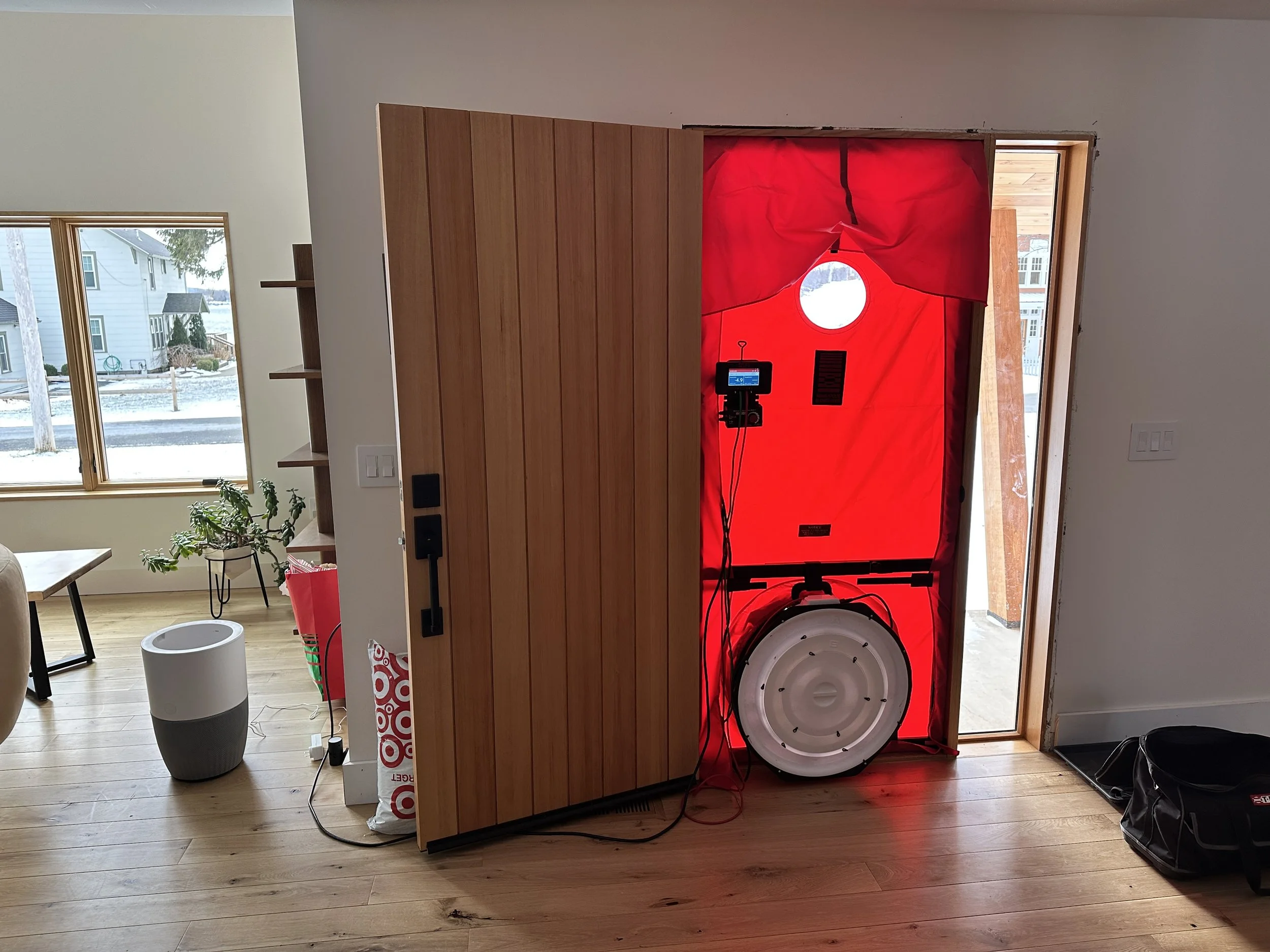 Large red canvas framework with a blower fan setup installed in a home doorway, beside the open wooden front door and snowy outdoor scene.