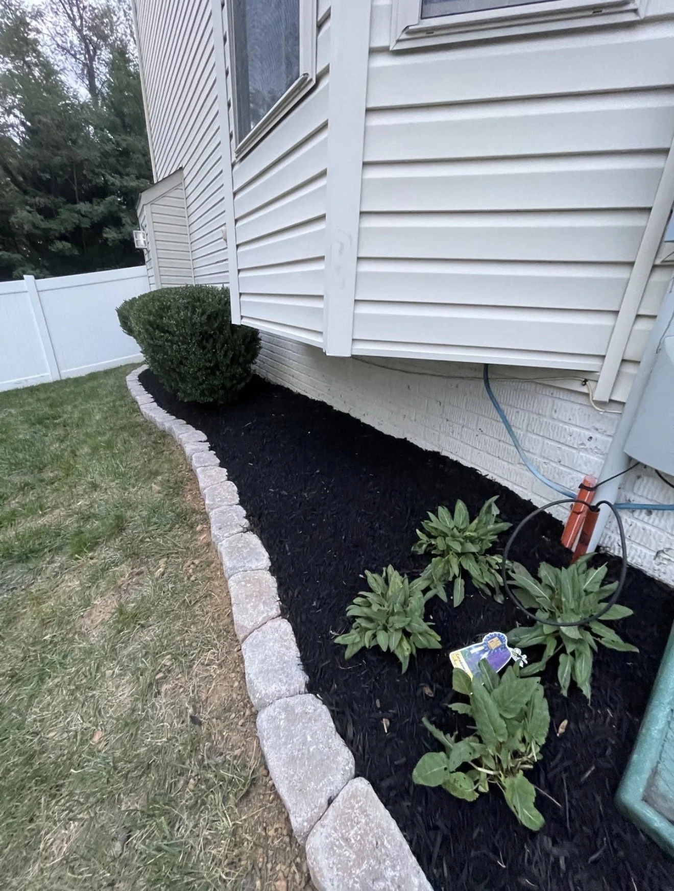 Mulching: fresh dark mulch in a stone-edged planting bed beside a home.