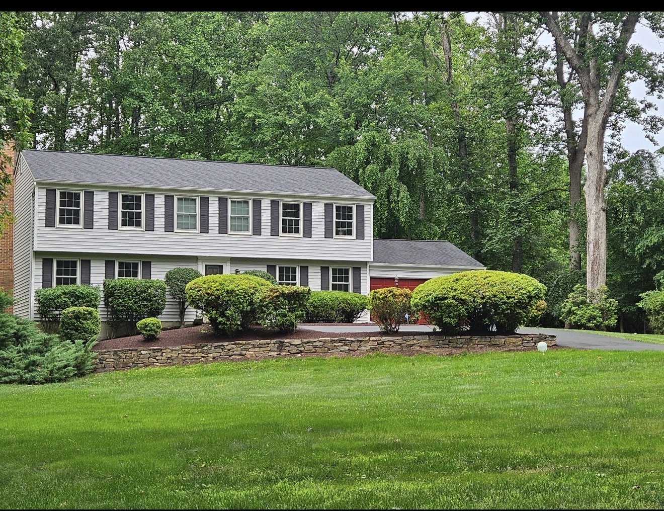Manicured lawn, mature trees, shaped shrubs, and a stone-bordered planting bed