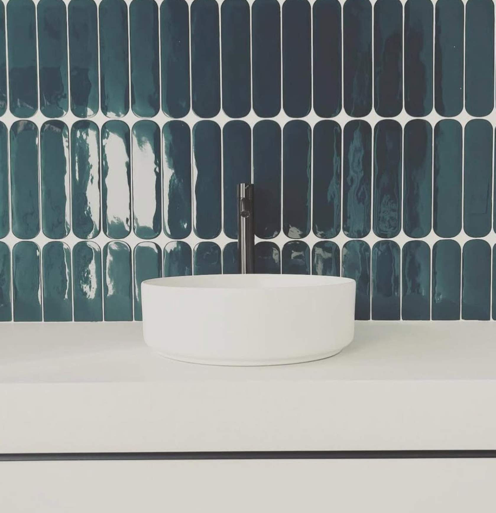 Lavabo blanc moderne avec robinet mural devant un carrelage bleu pétrole texturé.