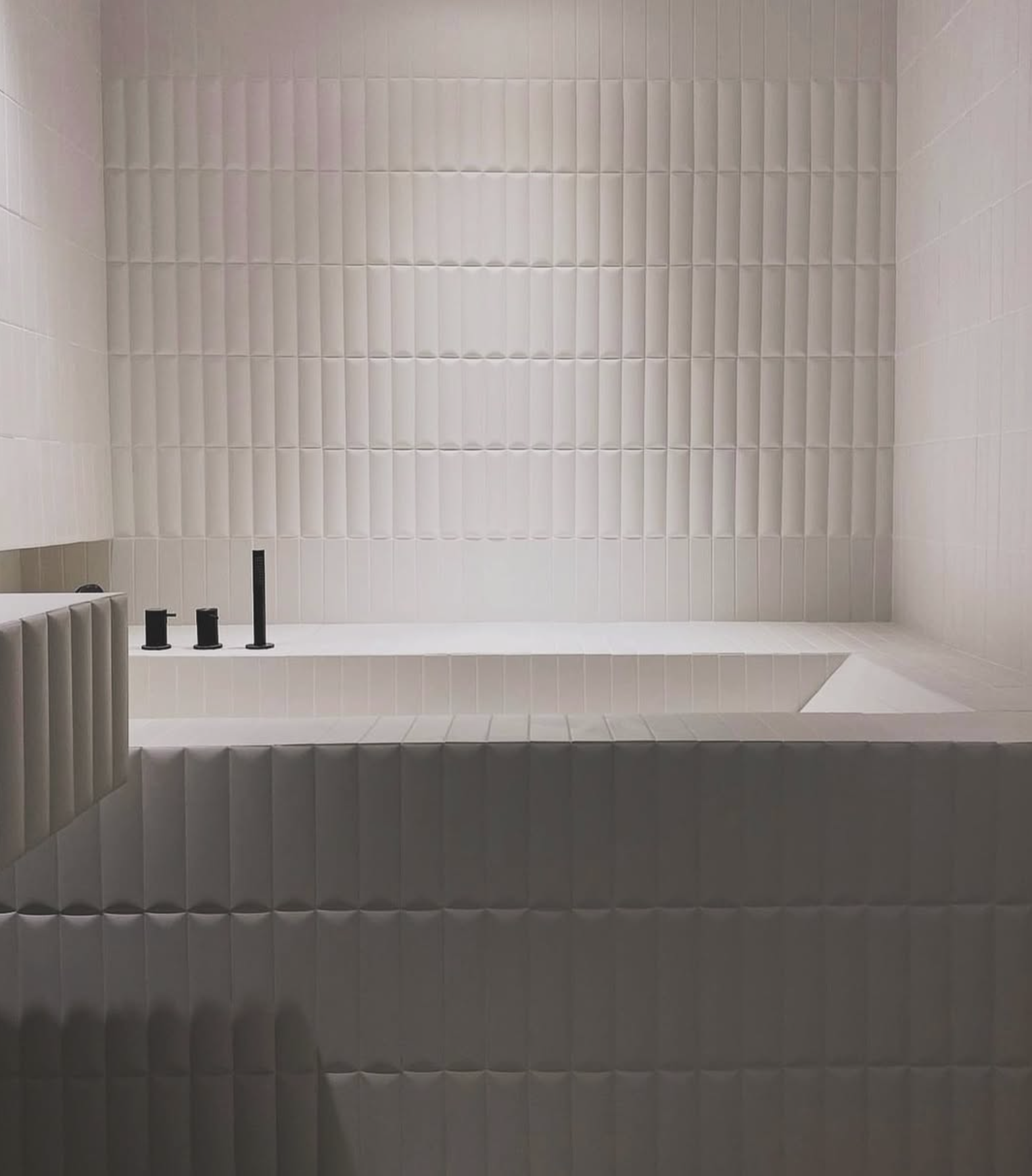 Baignoire moderne encastrée avec robinetterie noire, entourée de carrelage blanc texturé.