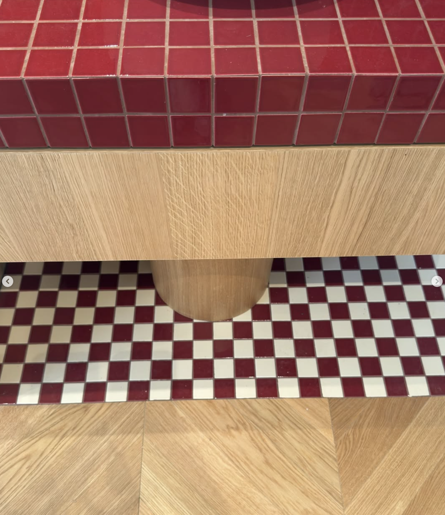 Banquette en bois devant un mur carrelé rouge, avec sol à damier rouge et blanc.