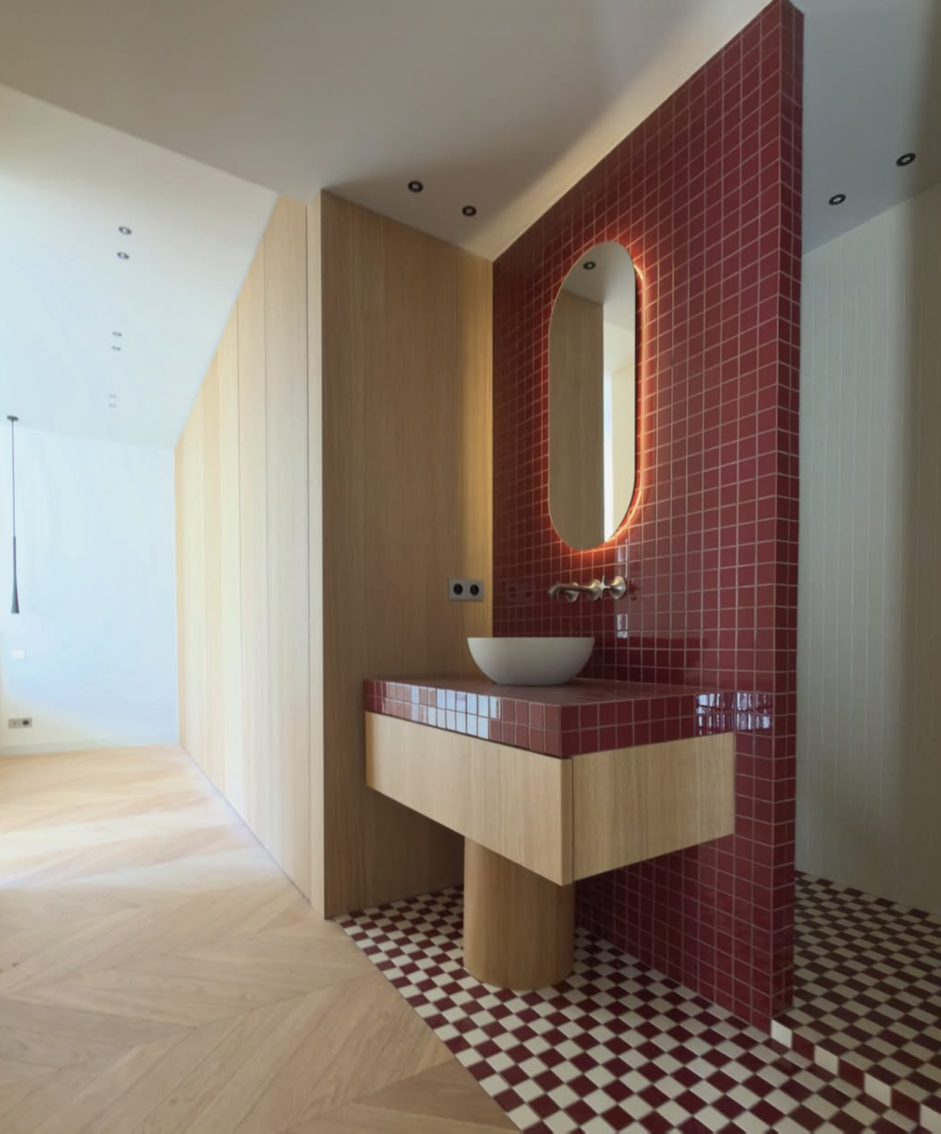 Salle de bains moderne avec lavabo vasque, miroir rétroéclairé, carrelage rouge et blanc à damier et meuble en bois.