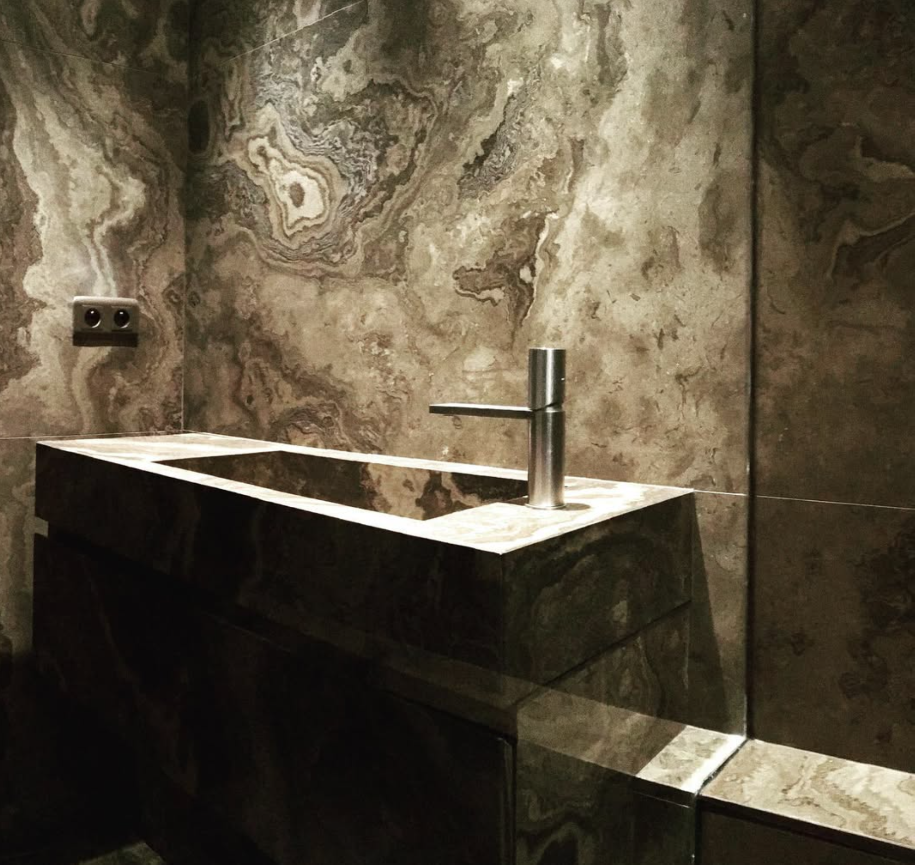 Lavabo contemporain en pierre marbrée sombre avec robinet cylindrique en acier inoxydable.
