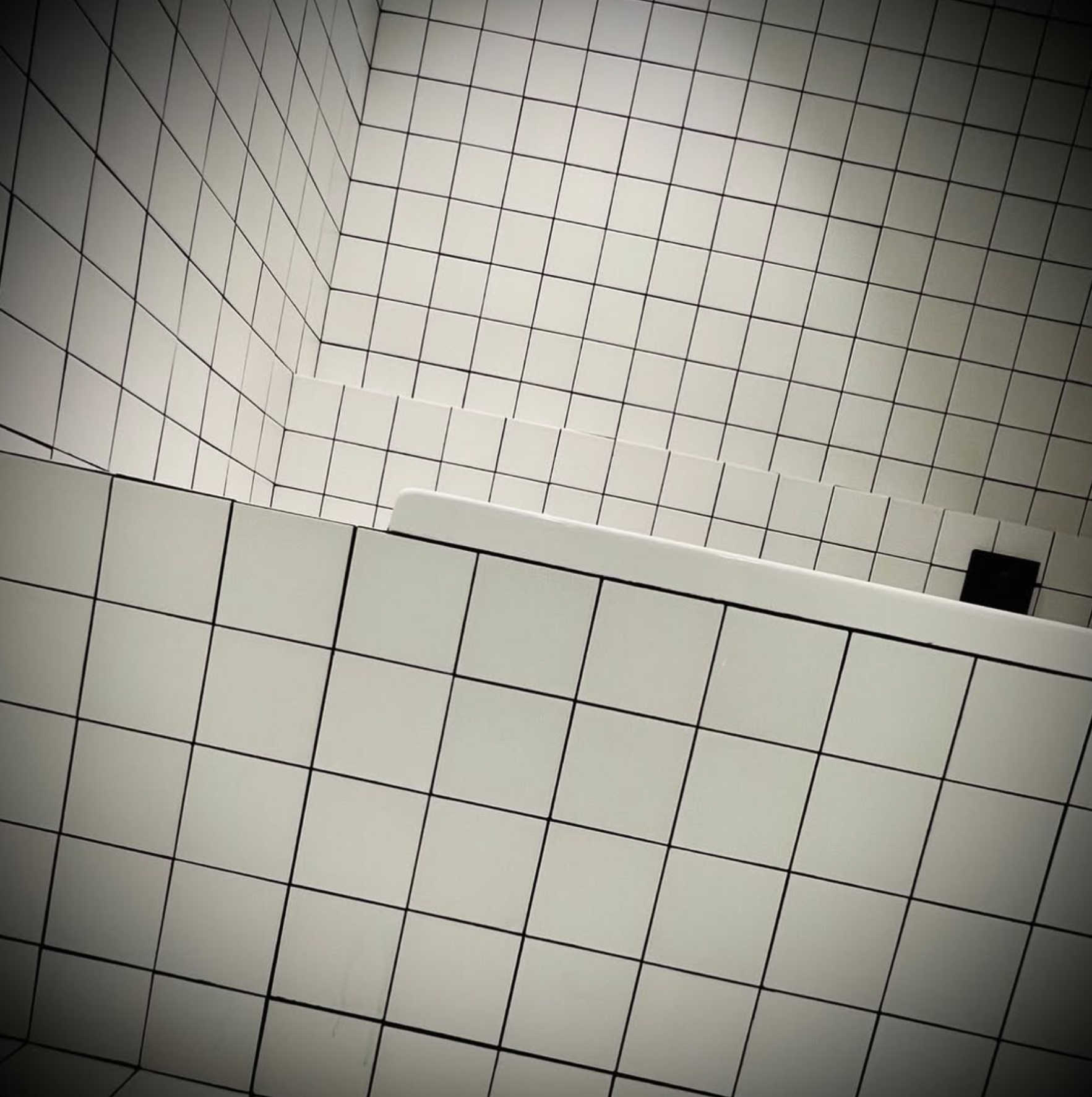 Salle de bain carrelée de blanc avec une baignoire et un robinet noir.