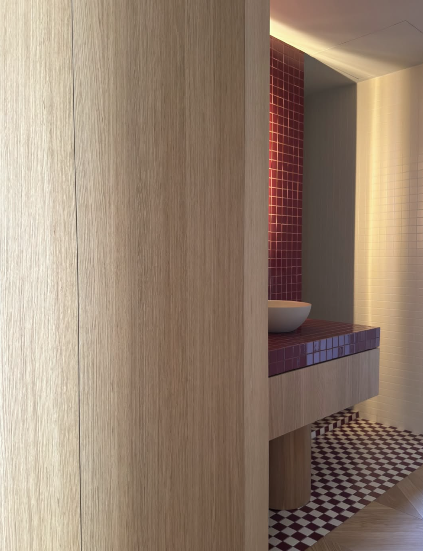 Salle de bains moderne avec meuble-lavabo en bois, vasque blanche, carrelage rouge et blanc et sol à damier.