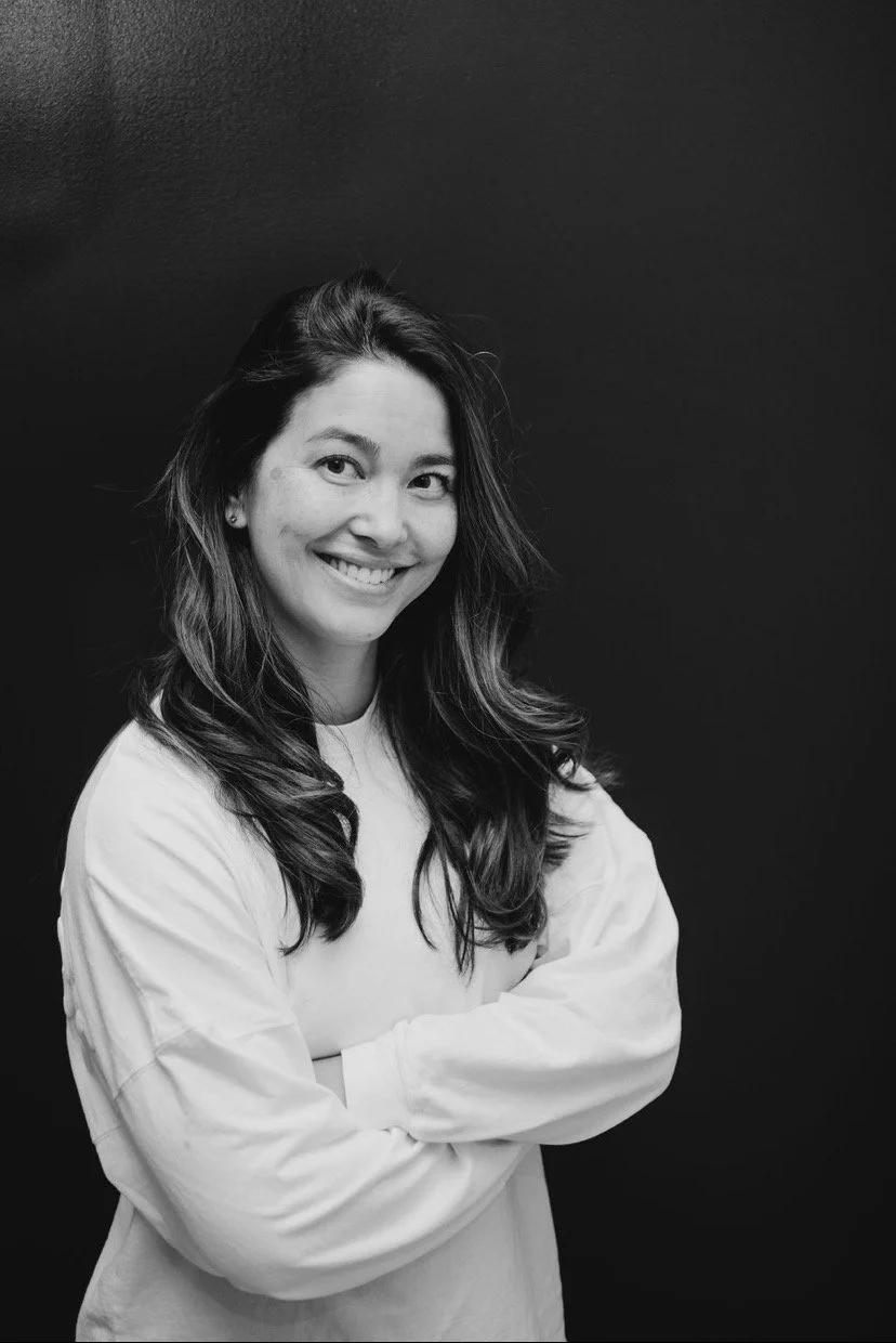 Black-and-white portrait of a smiling woman with long hair and folded arms against a dark background