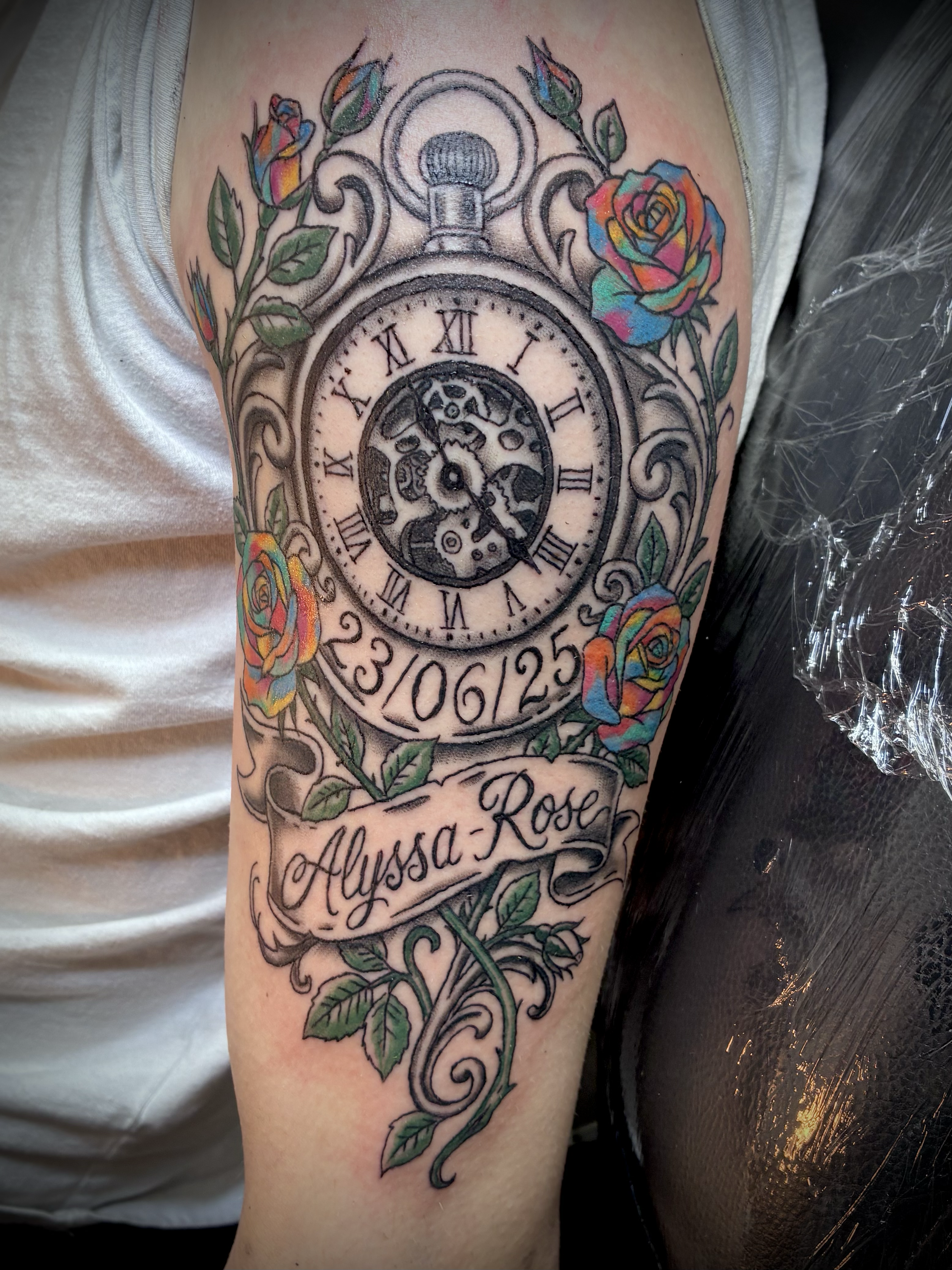 Black and grey pocket watch tattoo with colourful roses, decorative scrollwork, a personalised date and Alyssa Rose lettering.