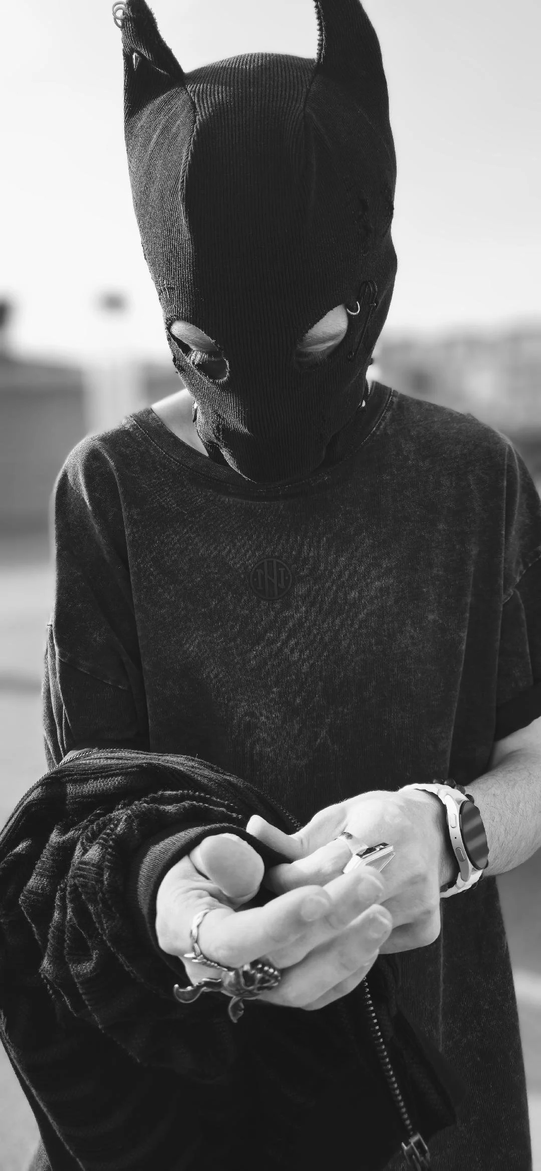 Person wearing a black knit balaclava with pointed ears and holding a smartphone in a black-and-white portrait