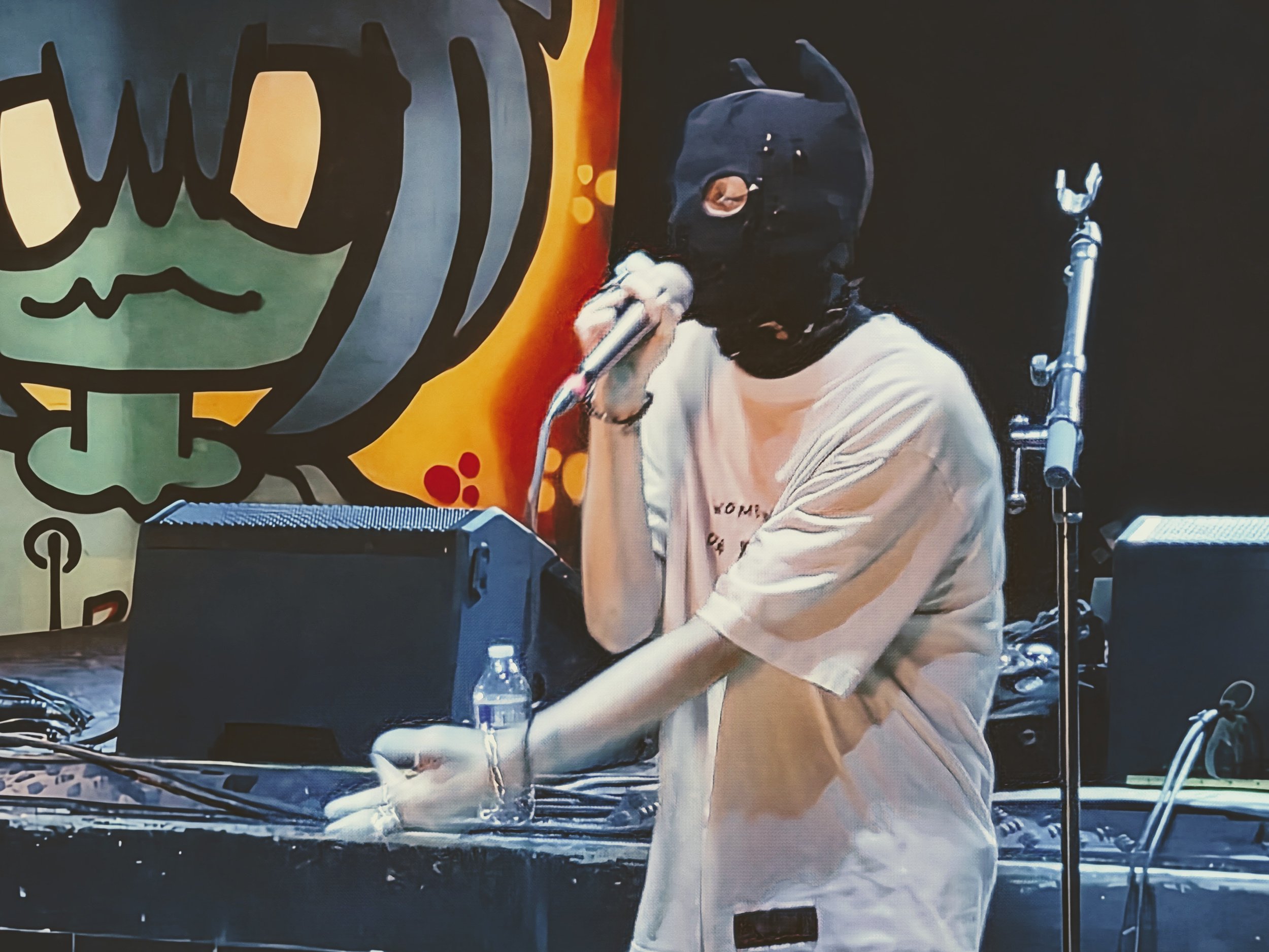 Masked singer performing into a microphone onstage in front of a colorful backdrop