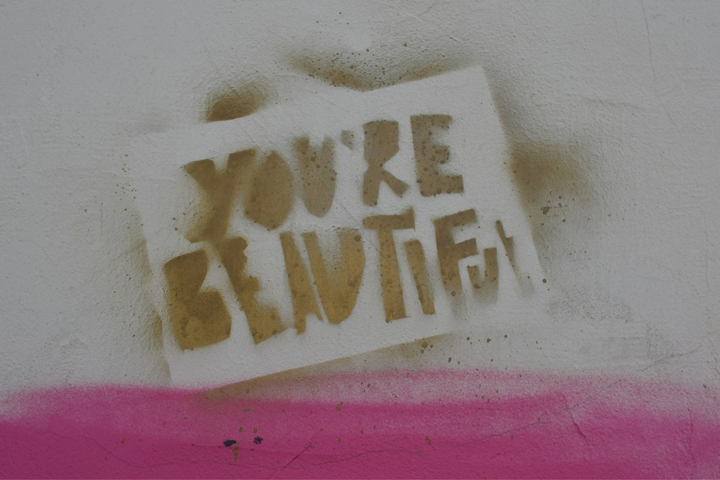 Close-up of weathered stencil graffiti reading “TOXIC” on a white and pink wall
