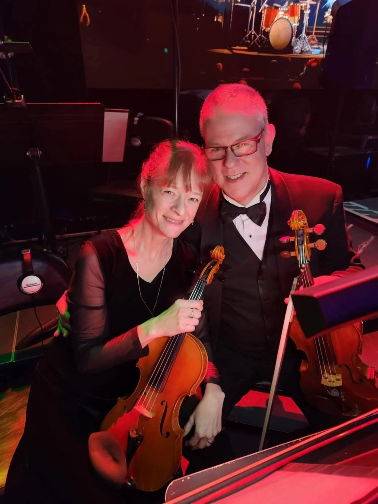 Two musicians posing with their cellos on a dimly lit stage.