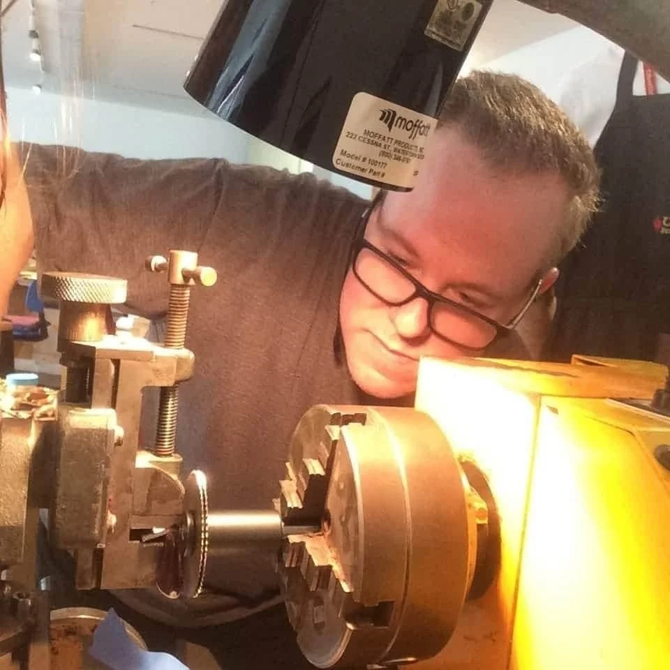 Person wearing safety glasses operates a metalworking lathe in a workshop.