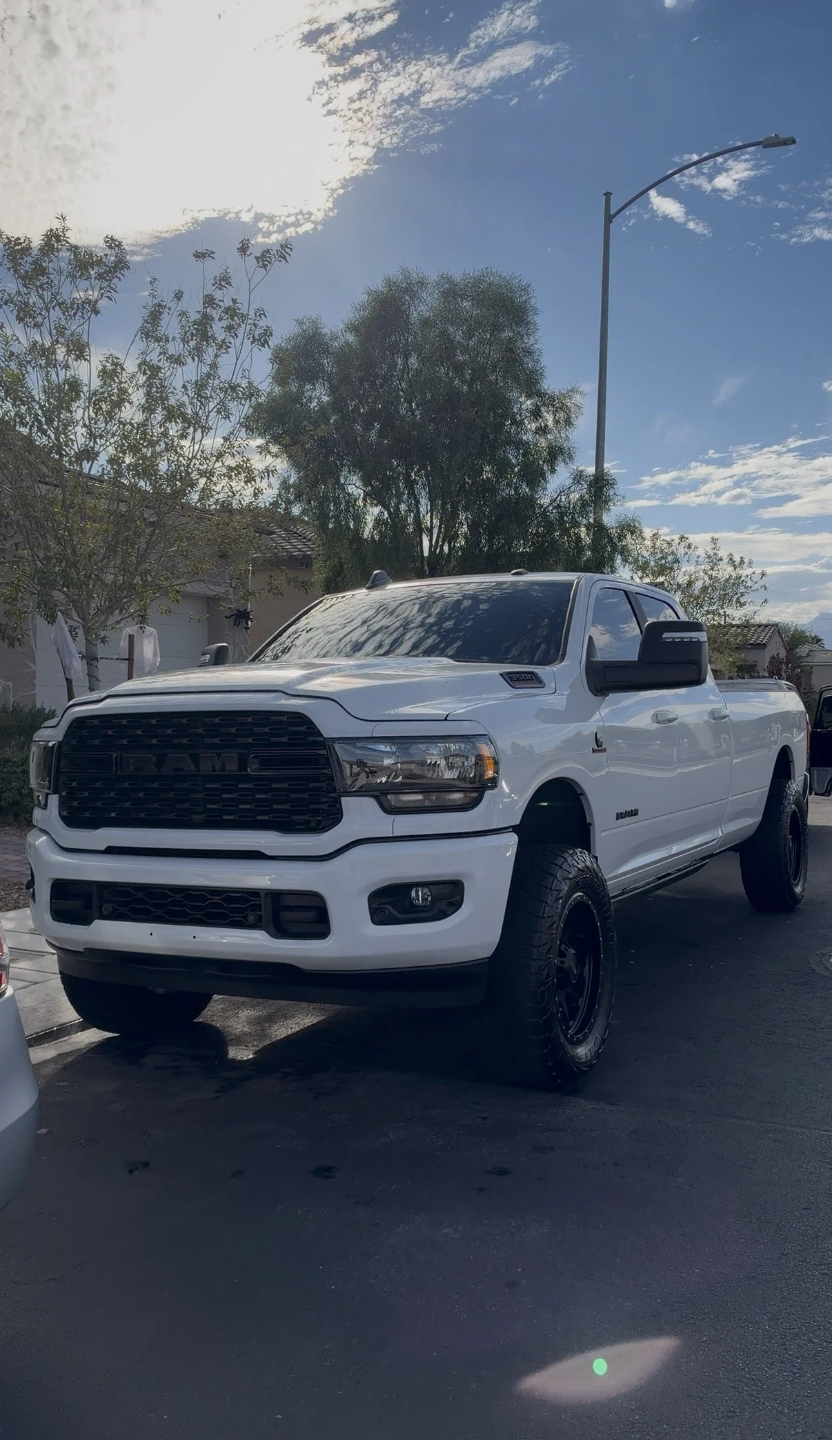 White Ram 1500 pickup truck with oversized tires parked in a residential driveway under a sunny blue sky
