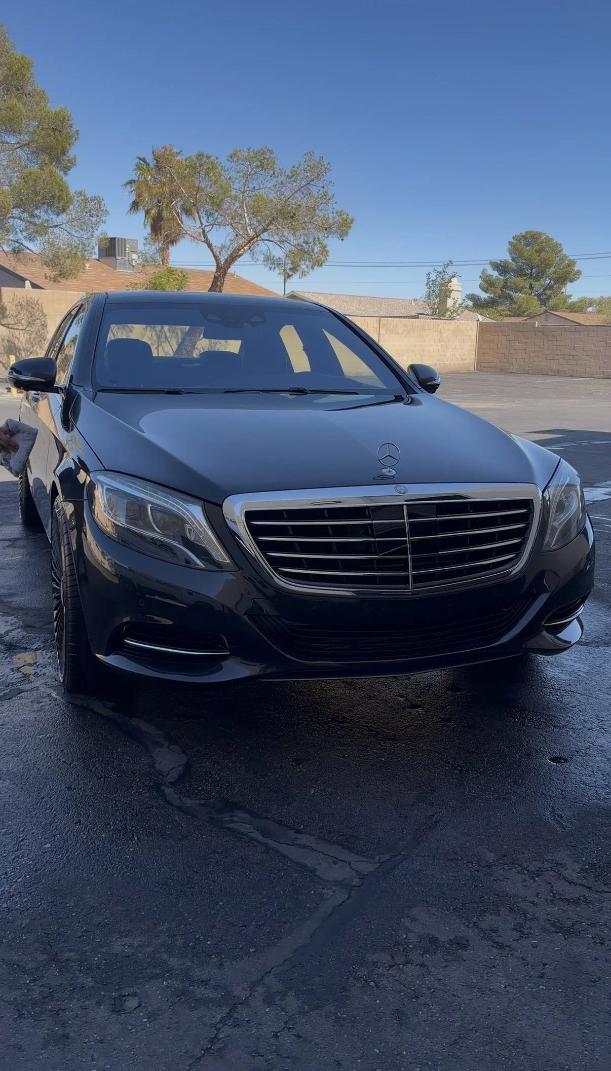 Front view of a black Mercedes-Benz luxury sedan parked on wet asphalt in a suburban driveway.