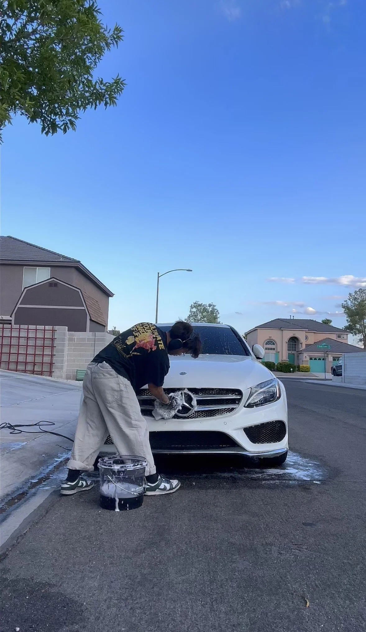 Person washing the grille of a white Mercedes-Benz sedan in a suburban driveway
