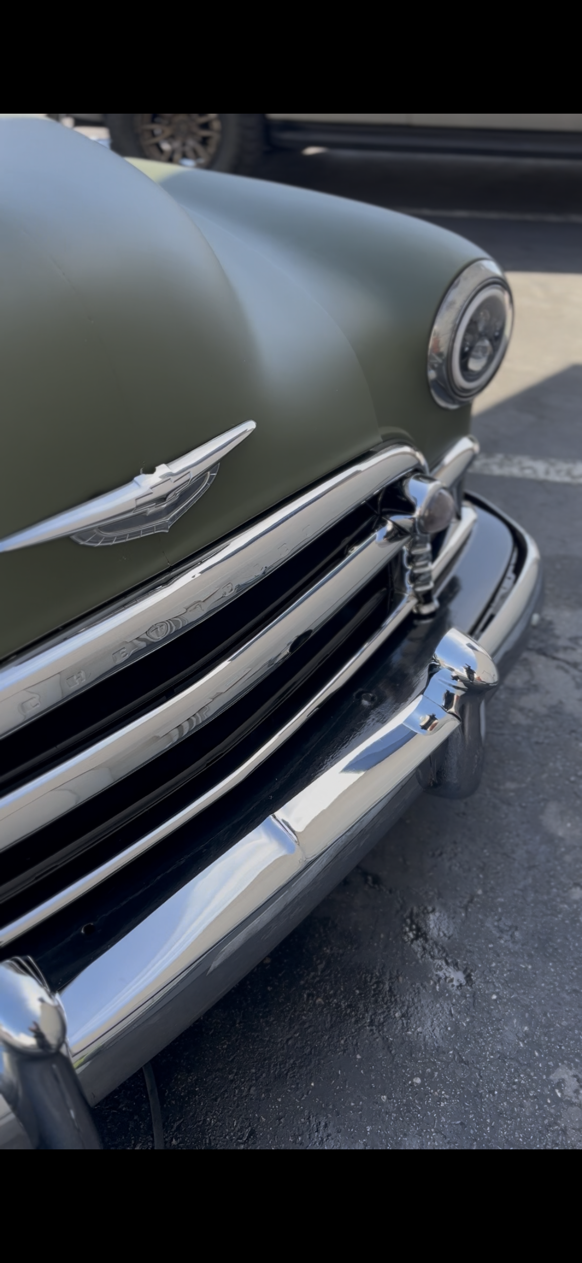 Close-up of a vintage olive-green Hudson automobile with chrome grille, hood ornament, headlight, and bumper.