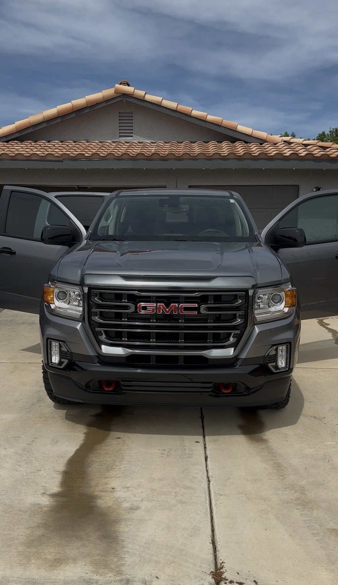 Front view of a dark gray GMC pickup truck parked in a residential driveway with its doors open.