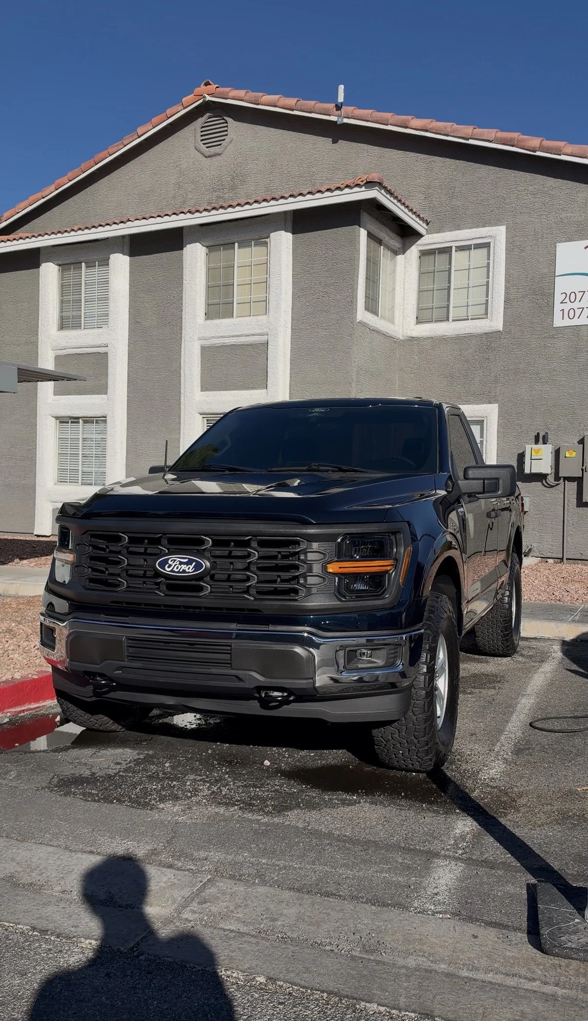 Black Ford pickup truck parked in front of a stucco building under a clear blue sky