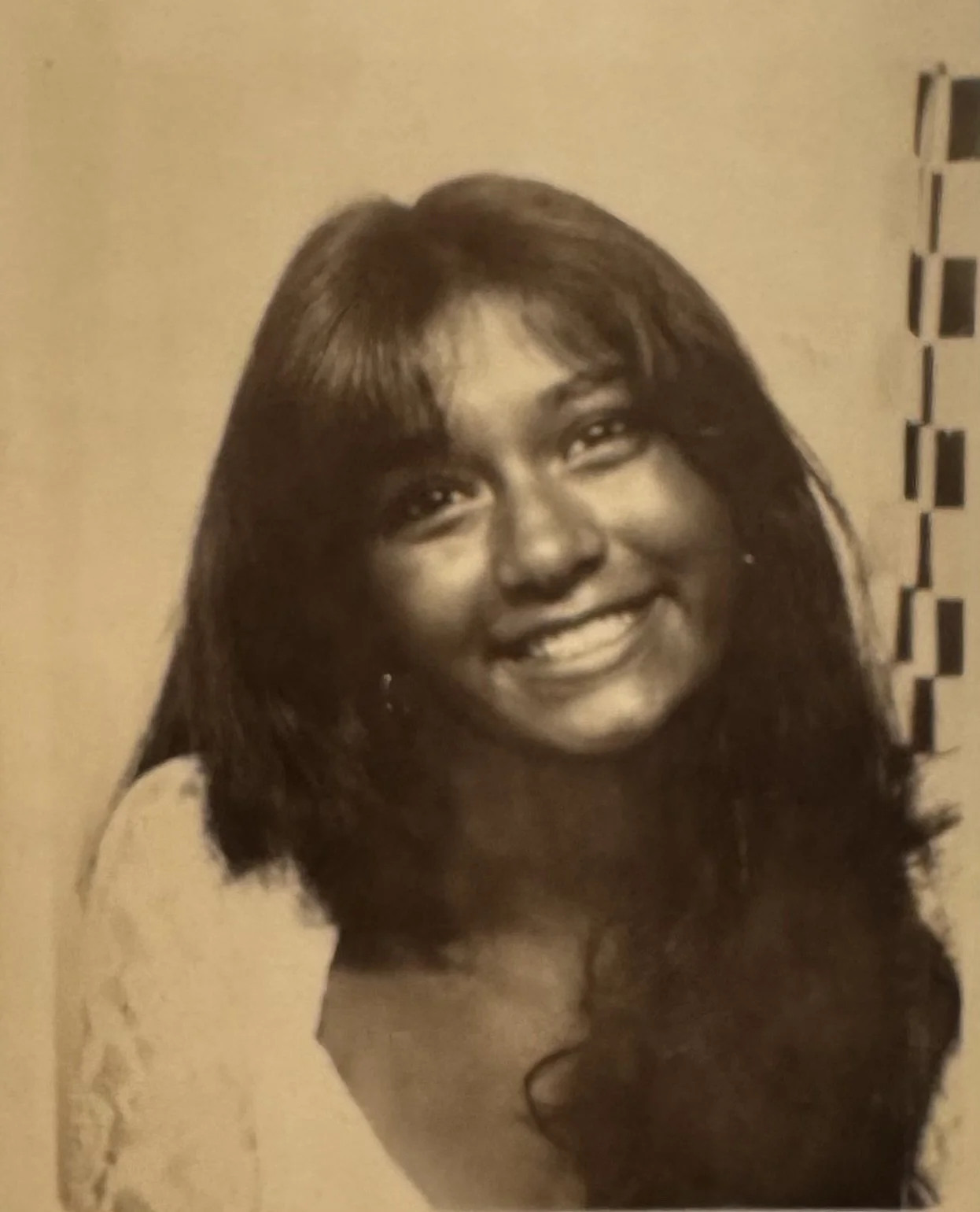 Sepia-toned portrait of a smiling woman with long dark hair and bangs.