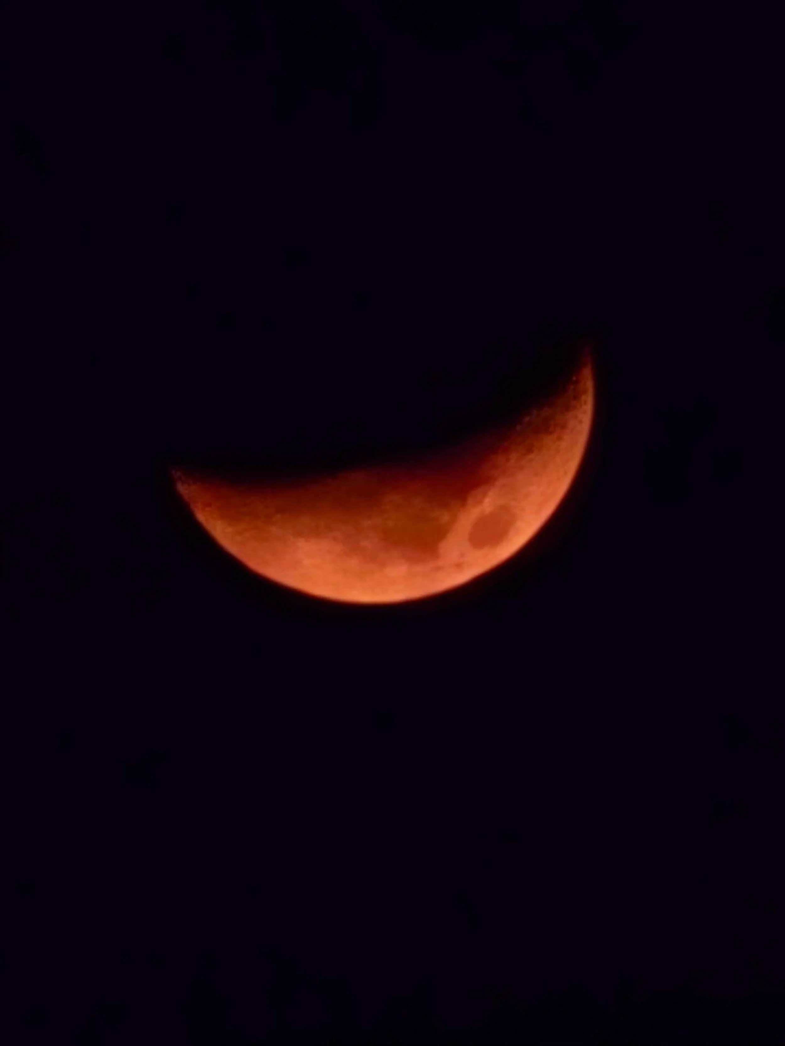 Close-up of a glowing orange crescent moon against a dark night sky