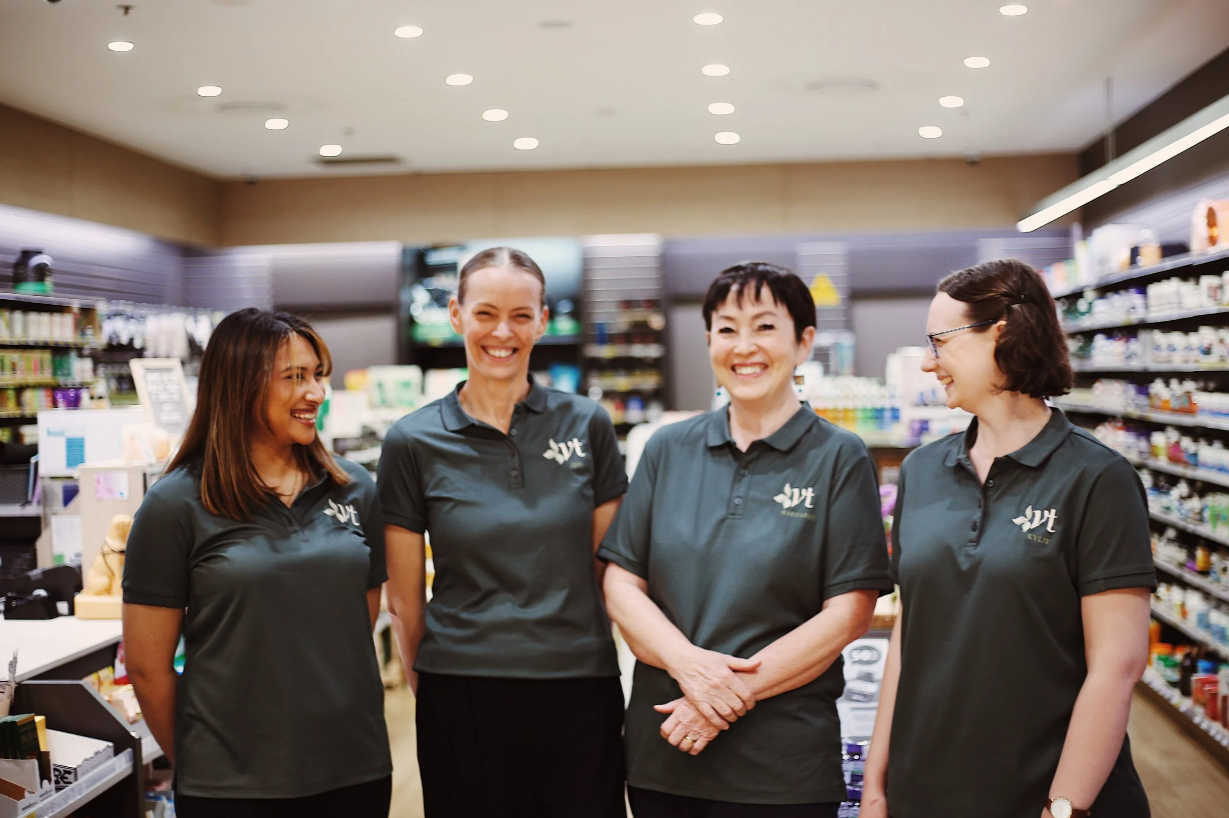 Four smiling health food store employees in matching polo shirts standing inside a health food store
