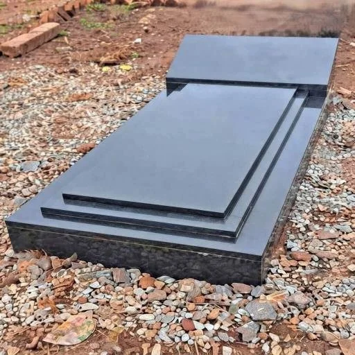 Polished black granite tombstone lying on a gravel-covered outdoor surface