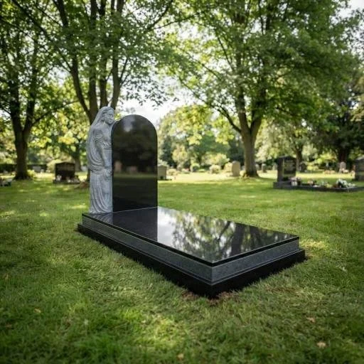 Polished black granite grave monument with a carved angel statue in a tree-lined cemetery