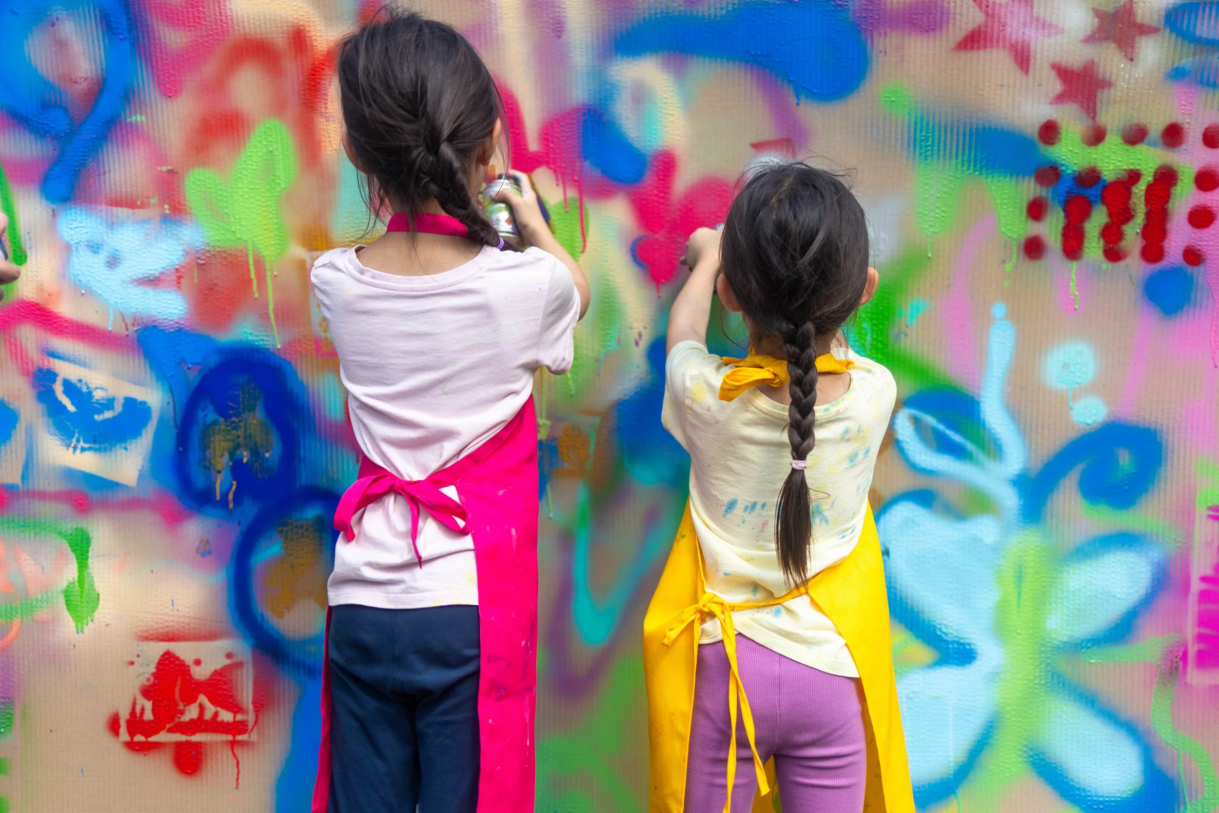 Two children in colorful aprons spray-painting a vibrant abstract mural. Photo by Jon Rees.