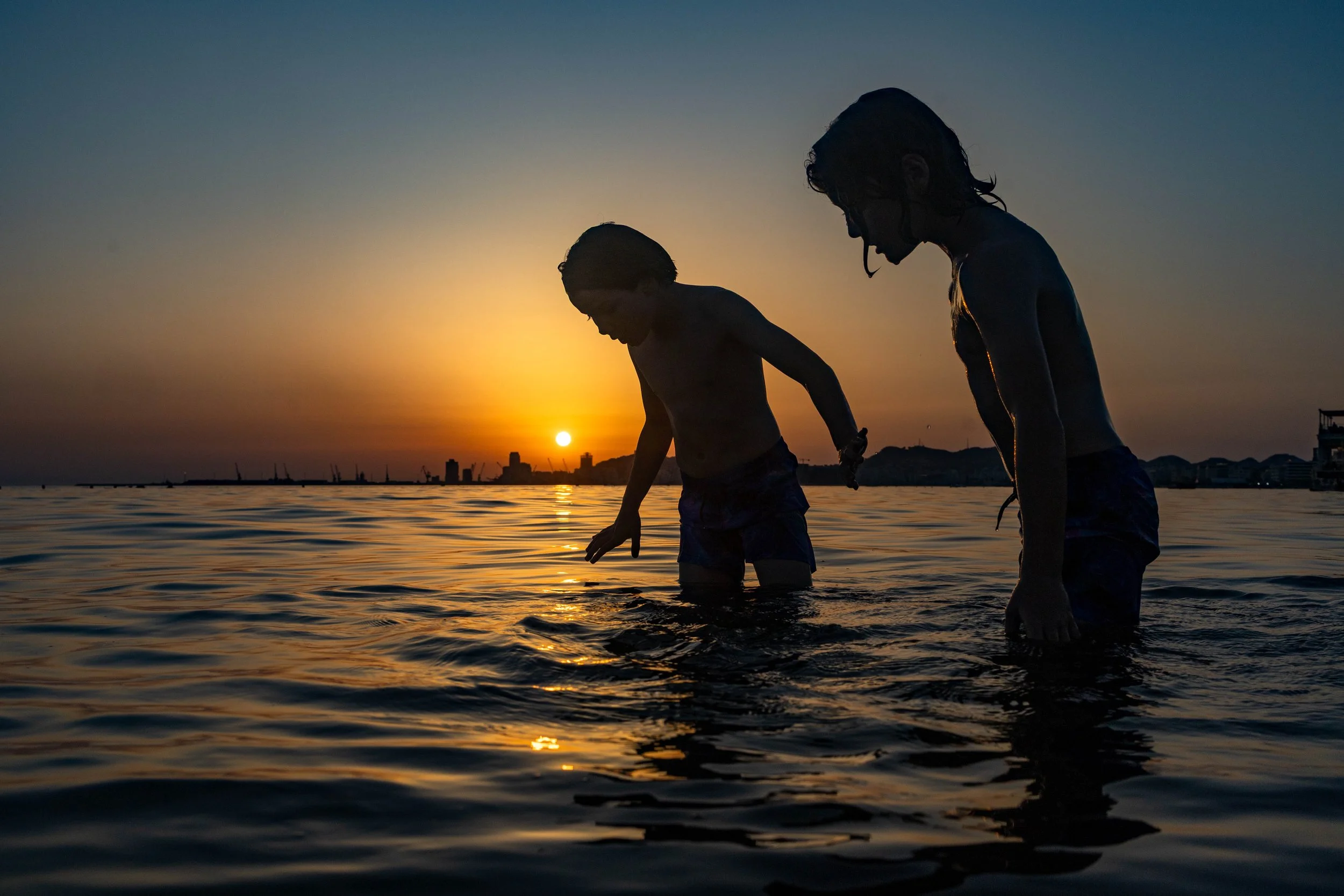 Silhouetted parent and child wading in the ocean at sunset. Photo by Jon Rees.